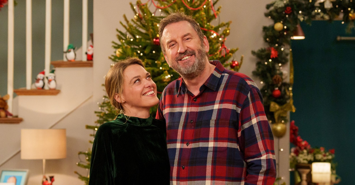 Lee Mack and Sally Bretton smiling in front of a Christmas Tree on not Going Out