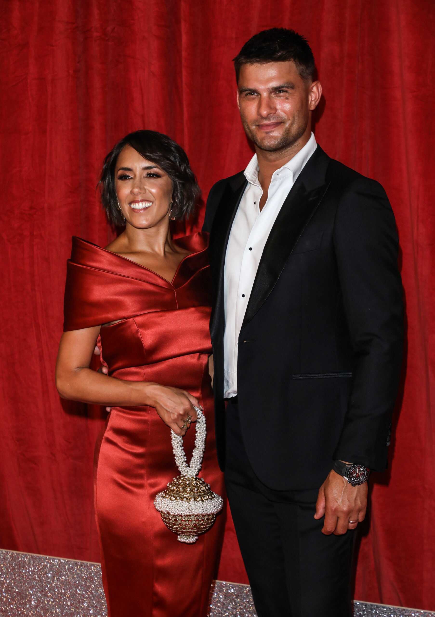 Janette Manrara and Aljaz Skorjanec smiling against a red backdrop