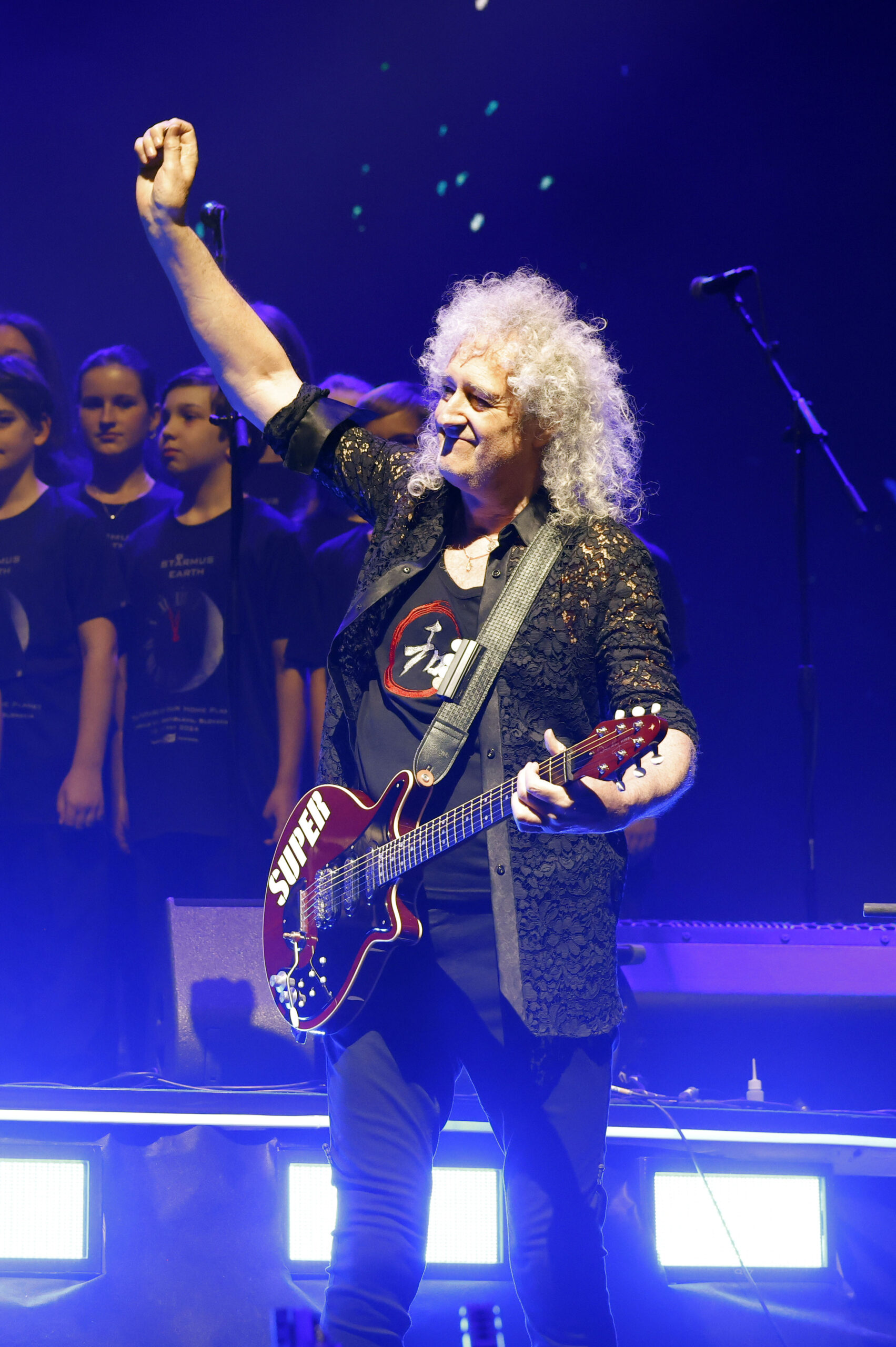 Brian May putting his fist in the air whilst on stage with guitar