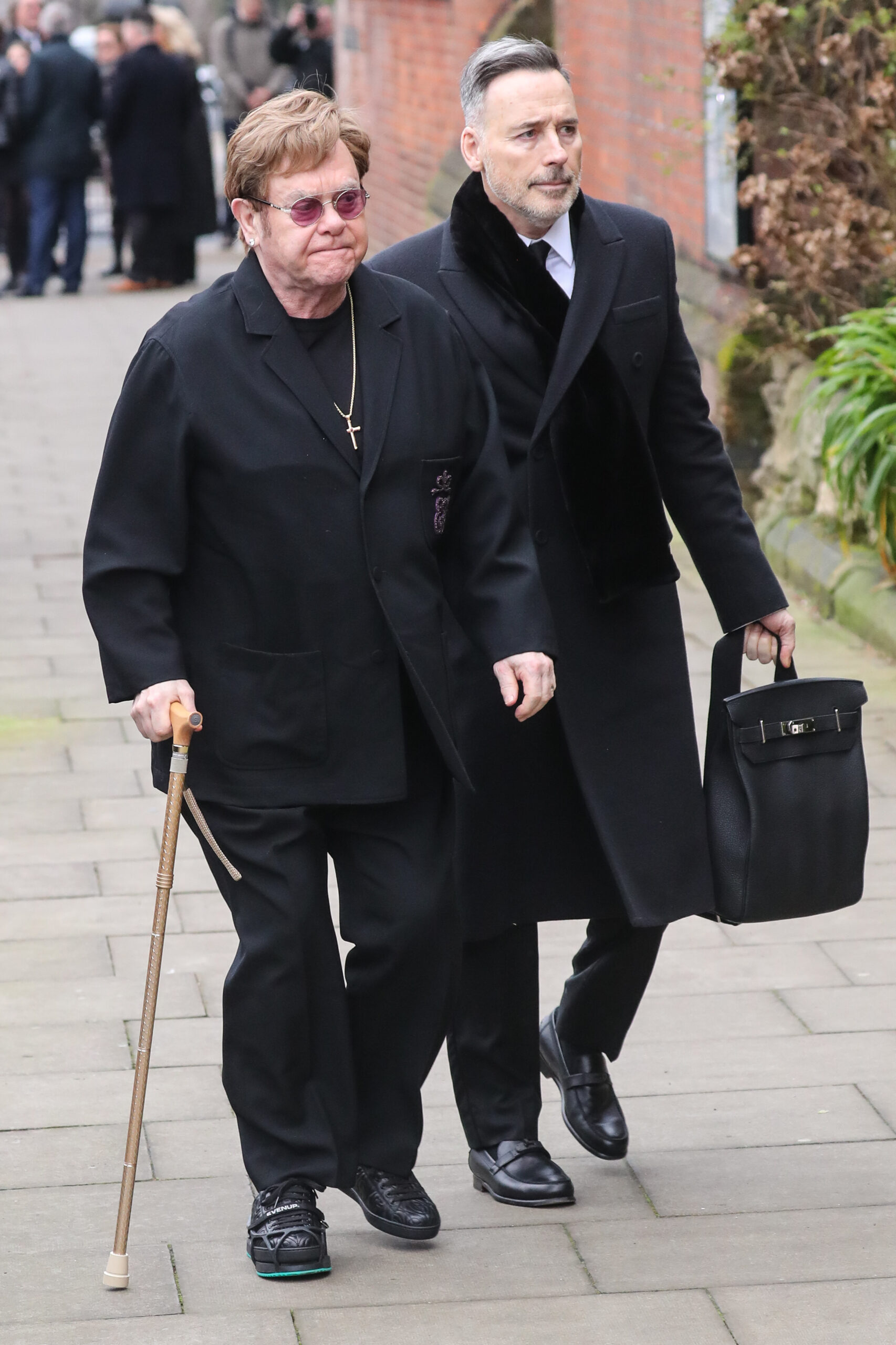 Elton John walking with stick alongside husband David Furnish