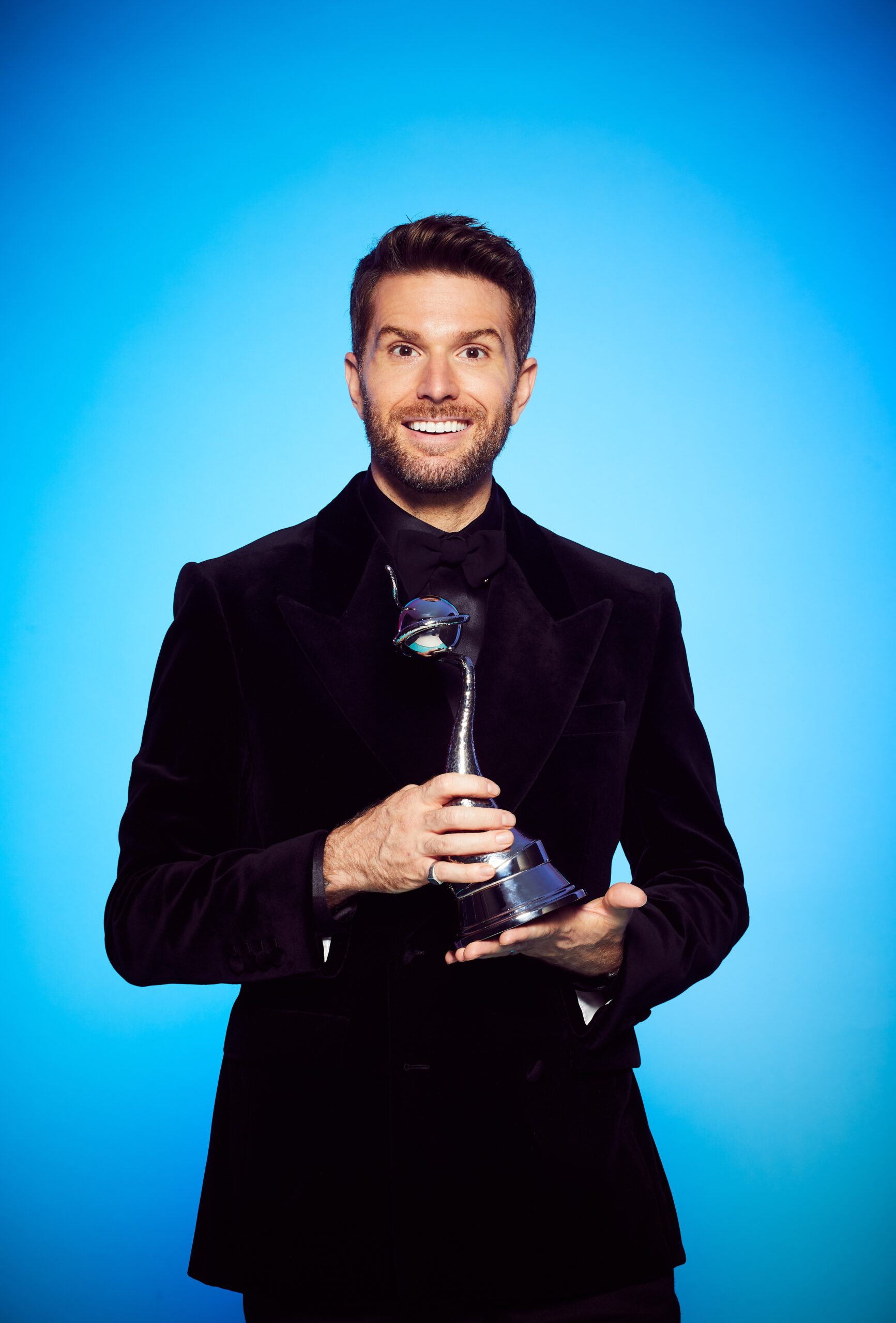 Joel Dommett holding an NTA in promo picture