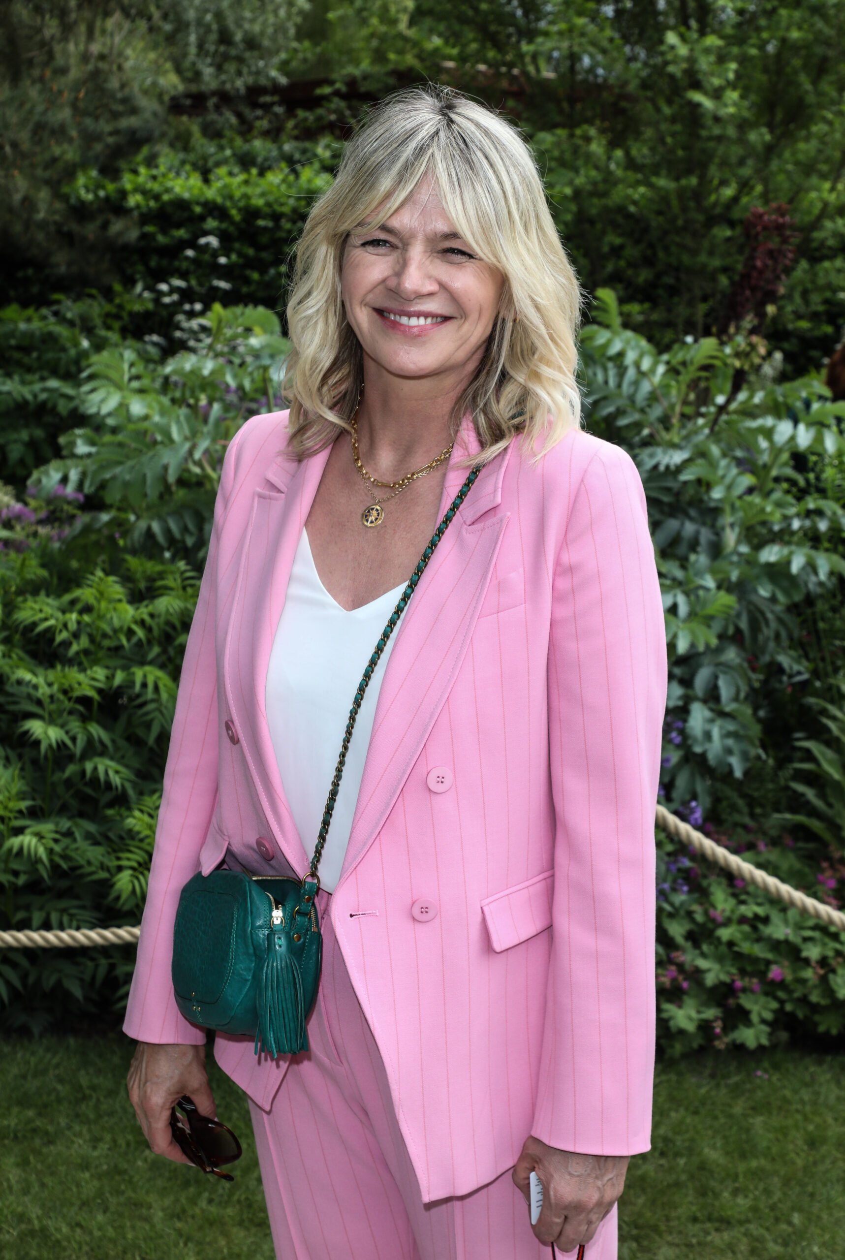Zoe Ball smiling in front of some shrubs