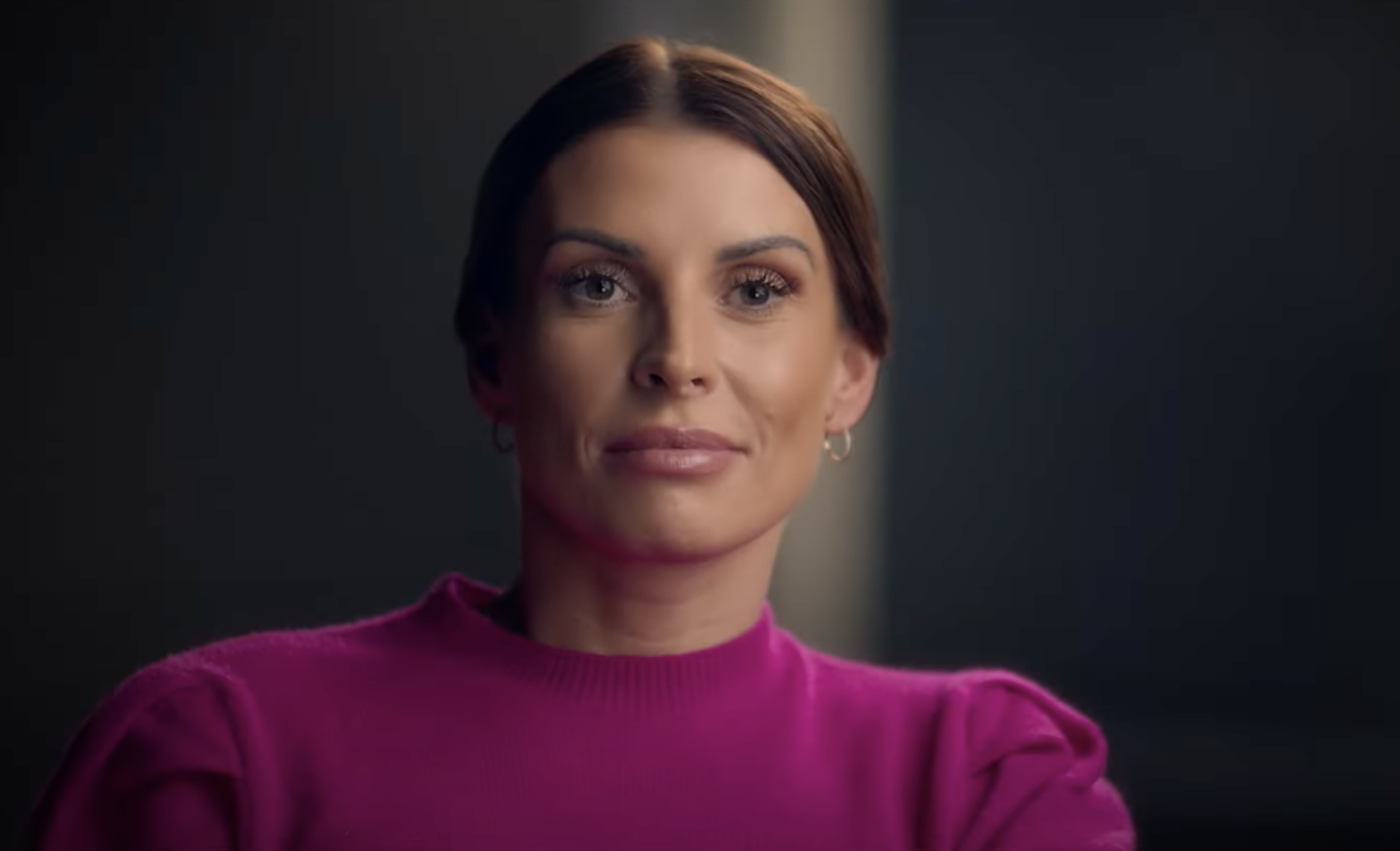 Coleen Rooney in a pink top looking just past the camera on the set of Hulu's The Real Wagatha Story