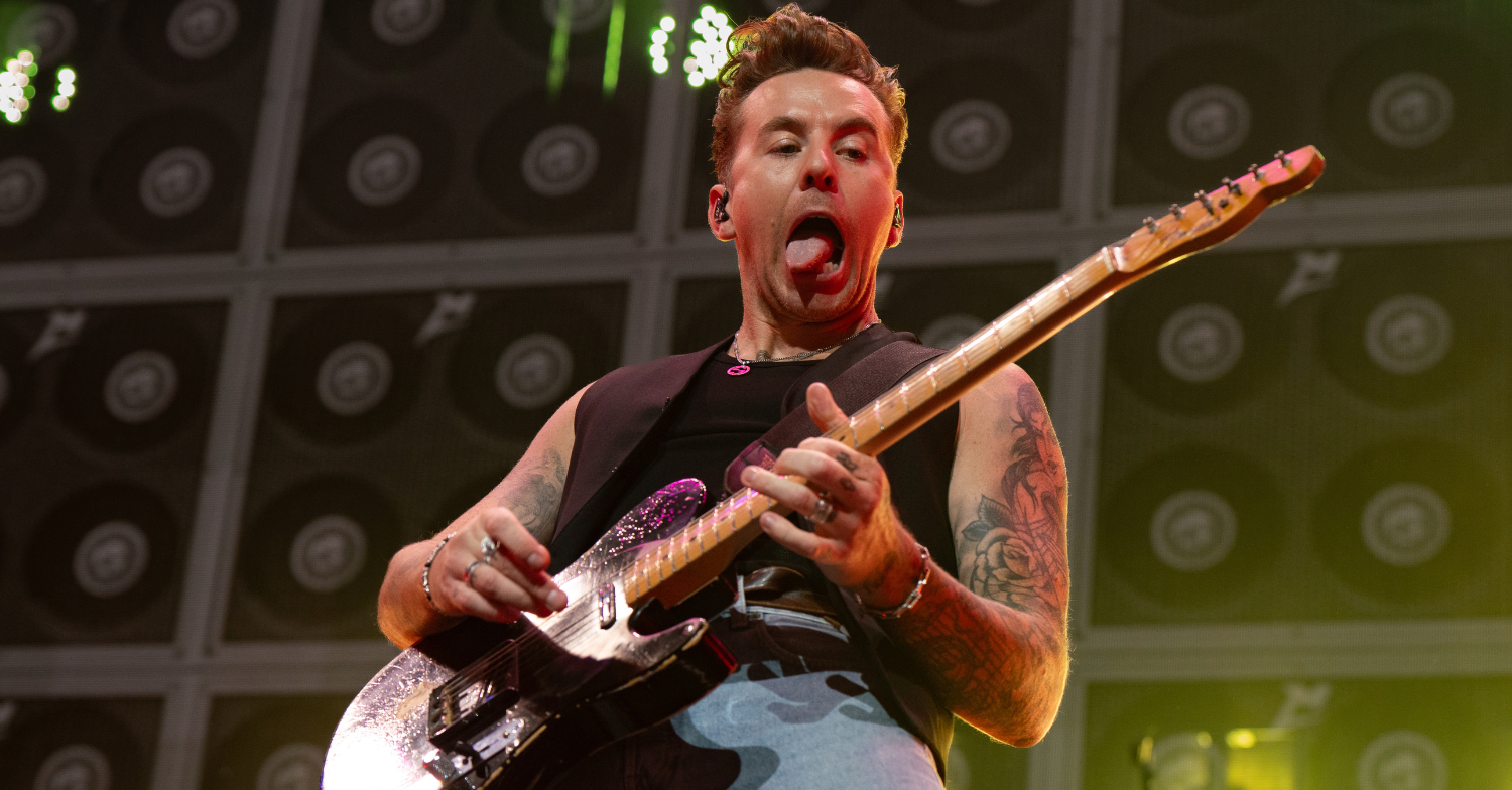 Danny Jones of McFly plays his guitar on stage and sticks his tongue out.