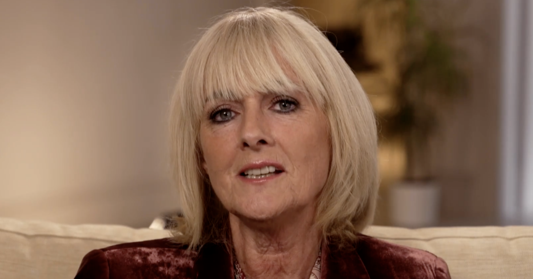 Jane Moore sitting on a sofa in a burgundy velvet jacket