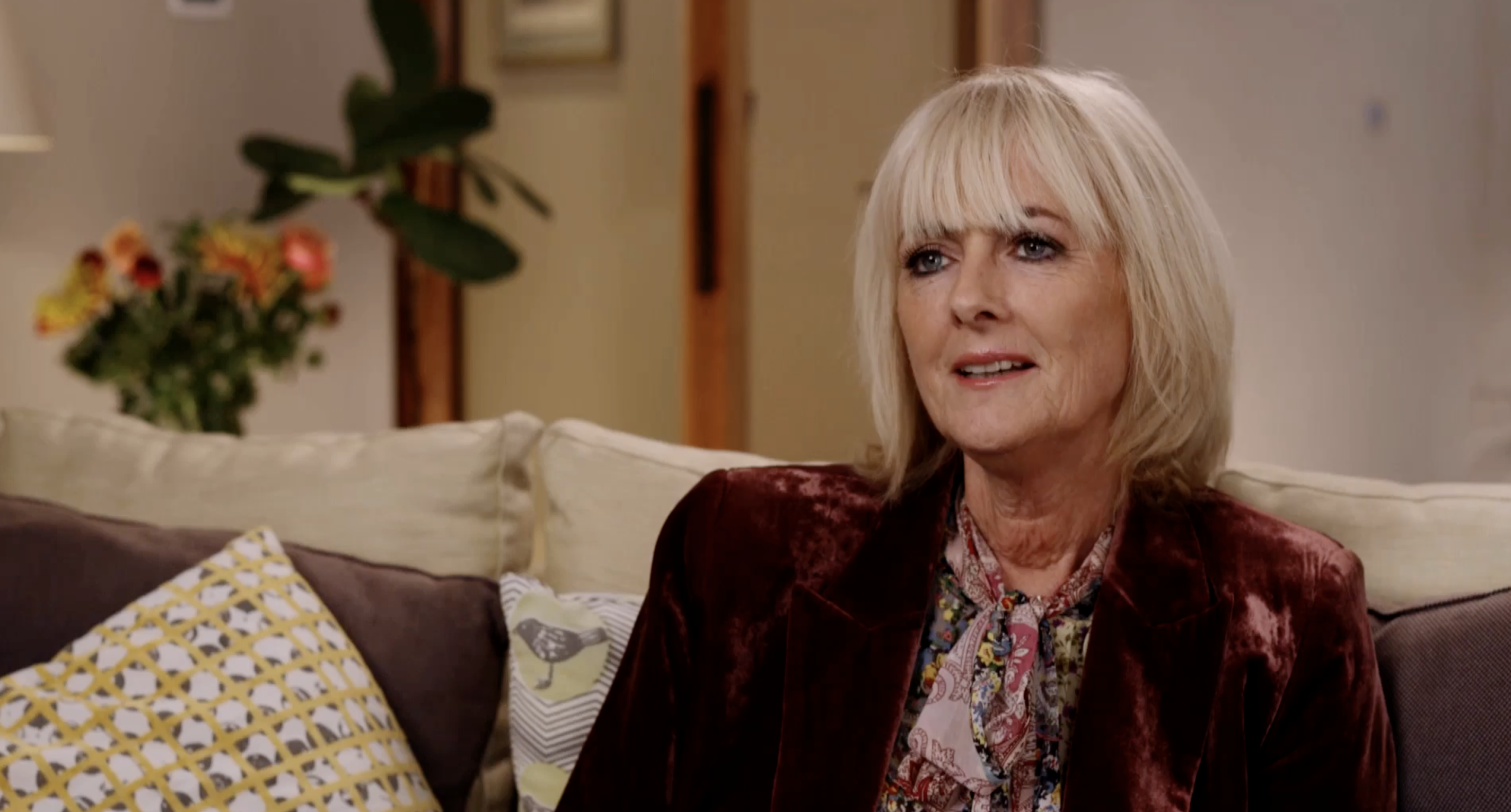Angled shot of Jane Moore sitting on a sofa in a burgundy velvet jacket for I'm A Celebrity