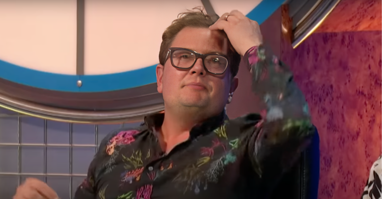 Alan Carr holds his hand to his head while wearing a floral shirt and sitting on the 9 out of 10 cats panel.