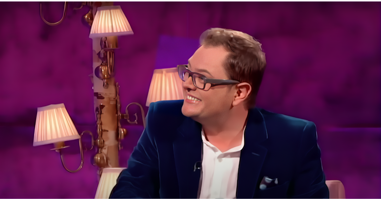 Alan Carr looks to the left wearing a white shirt and blue velvet jacket on Chatty Man.