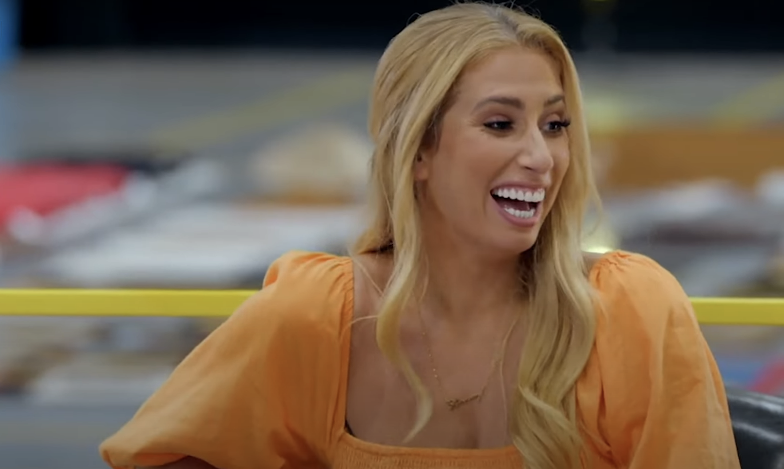 Stacey Solomon in an orange blouse laughing and turning her head to the side