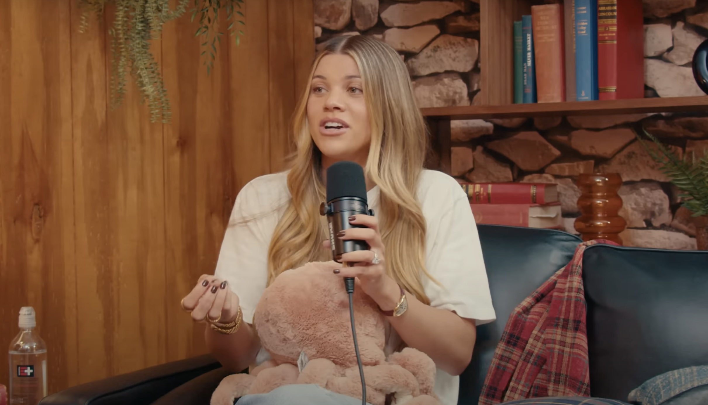 Sofia Richie sitting on a black leather sofa holding a microphone in her left hand