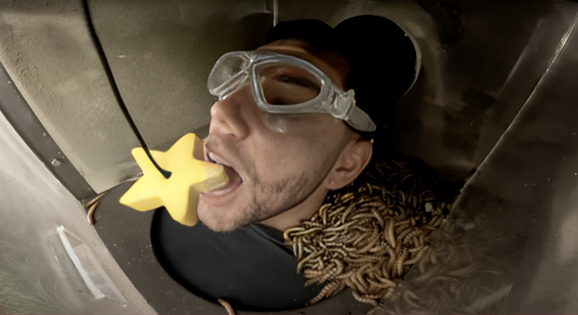 Dean McCullough bits on to a star while wearing safety goggles and trapped in a box of maggots during Bushtucker trial