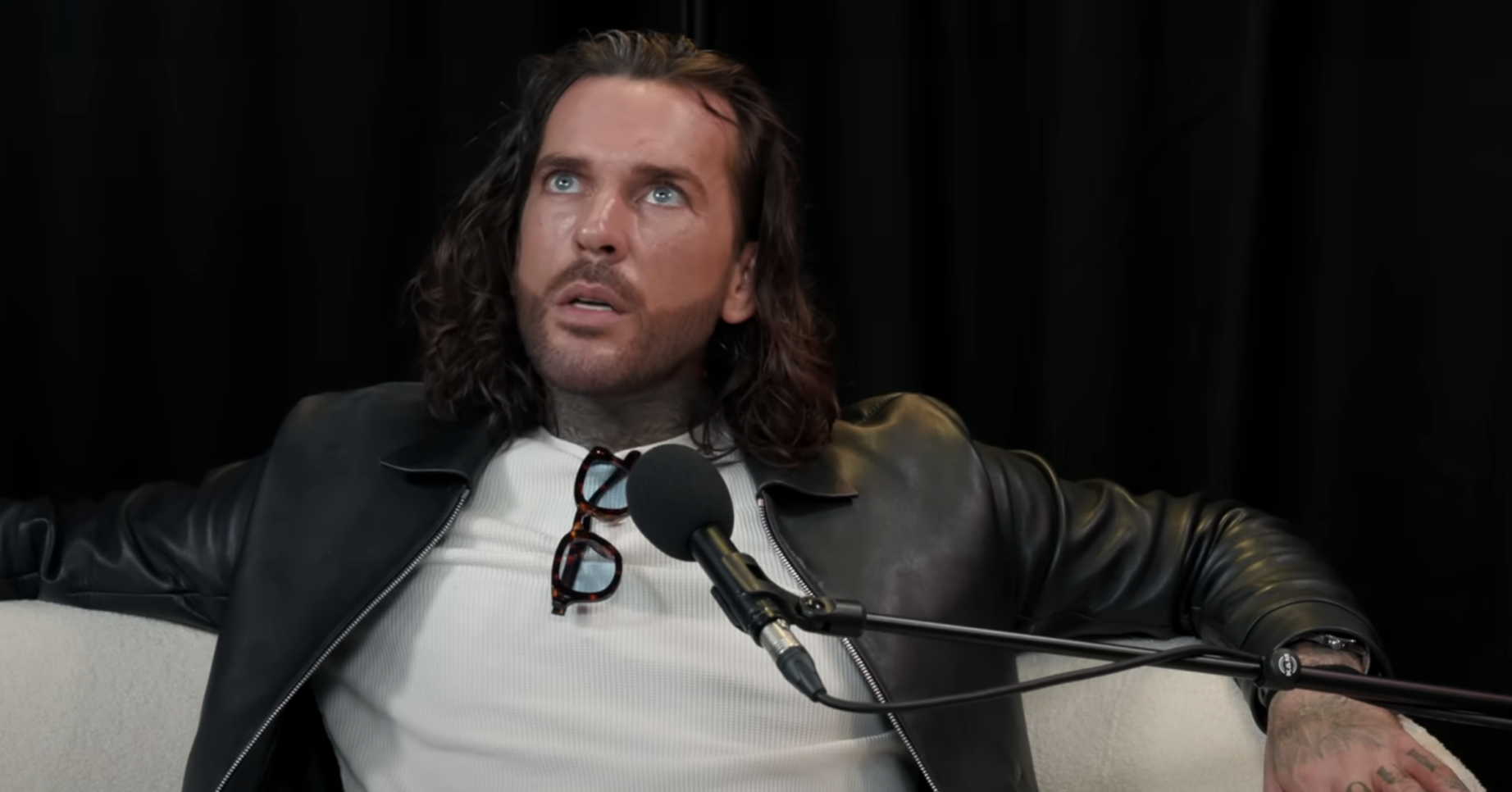 Pete Wicks in a leather jacket on the sofa with a studio microphone