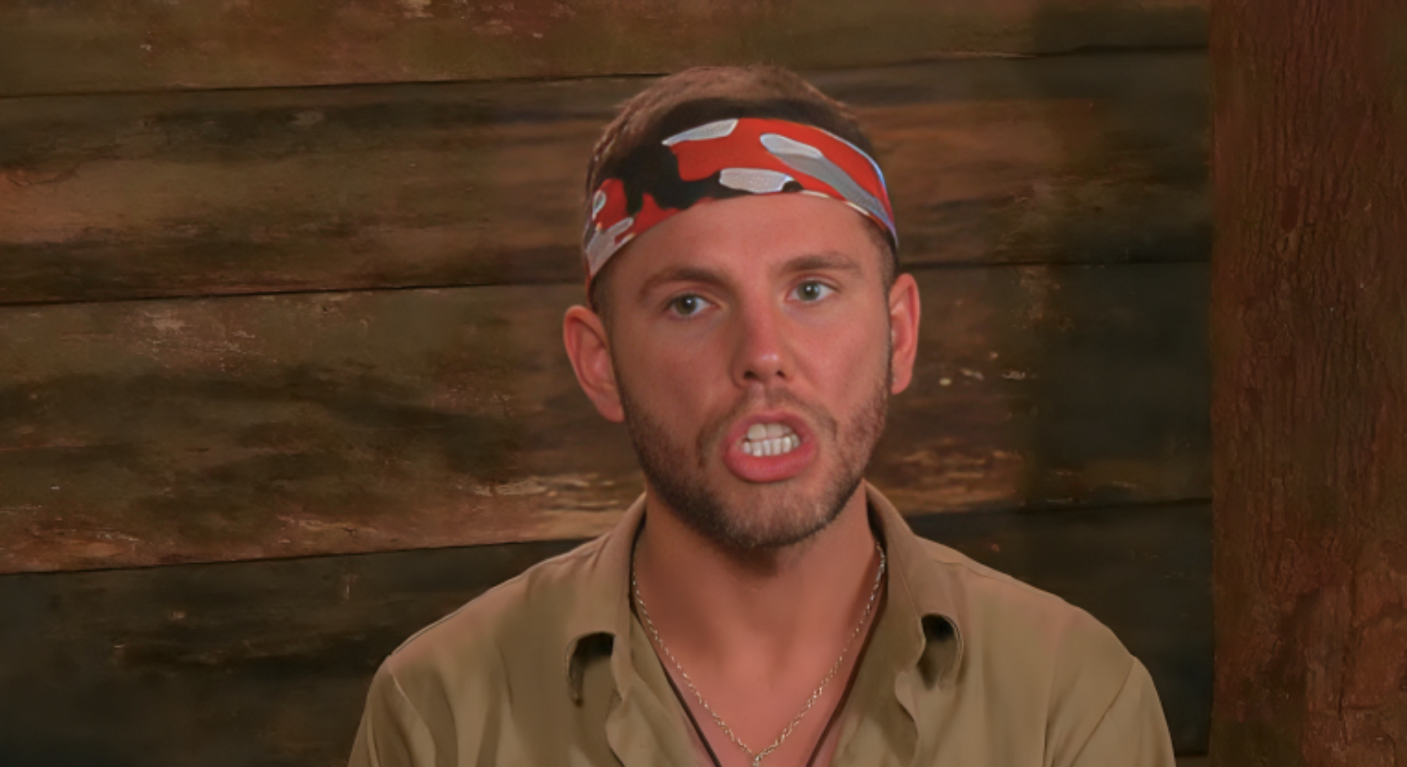 Dean is in confessional wearing a tan shit and a headband. He is complaining to the I'm a Celebrity crew.