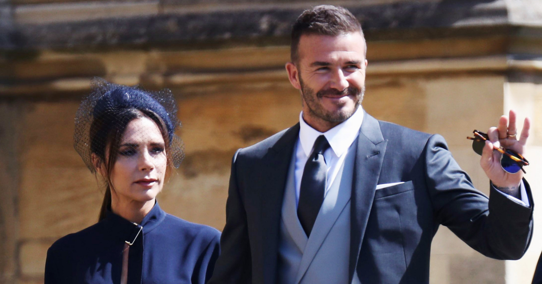 David Beckham waves at the camera while holding his wife Victoria's hand