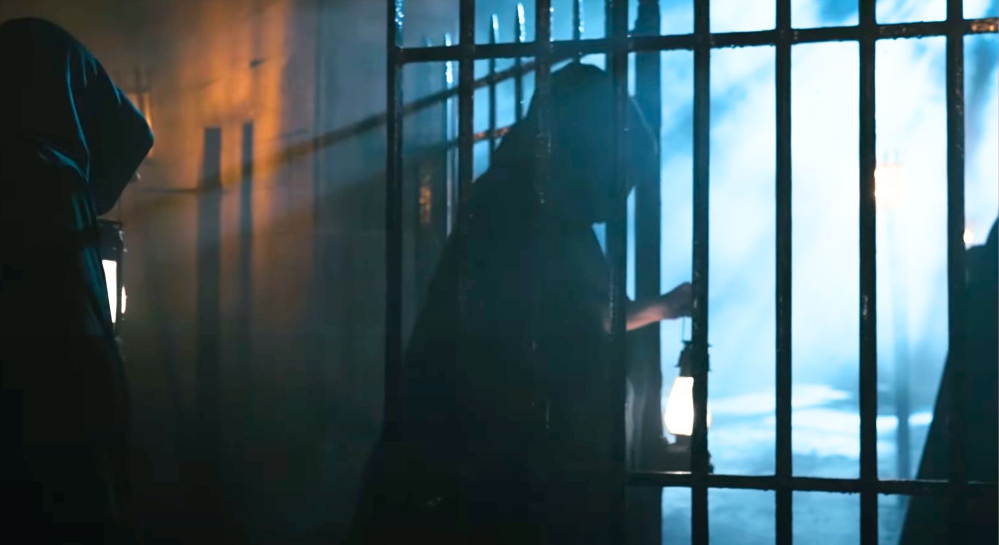 Still from The Traitors series 3 teaser trailer of a hooded figure holding a lantern and stepping through a backlit gate