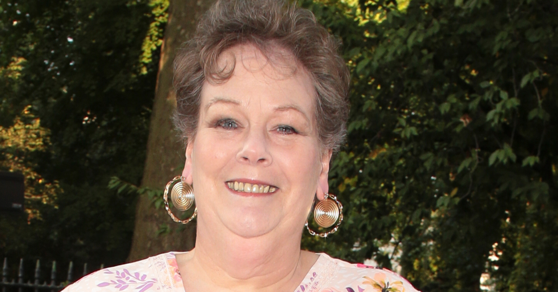 Anne Hegerty smiles for the camera clad in a white dress, matching her outfit with gold earrings
