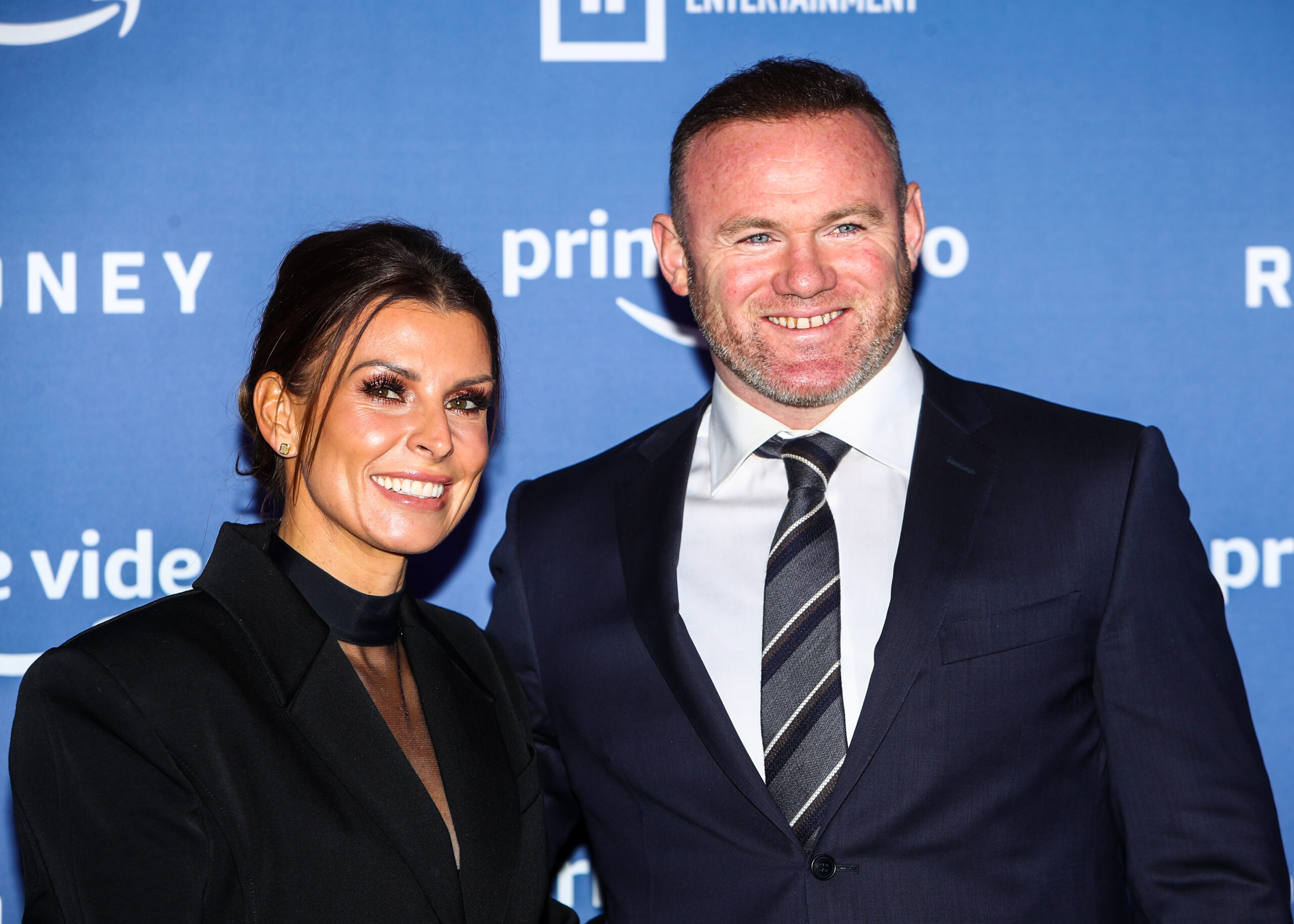 Coleen and Wayne Rooney stand beside each other smiling for the cameras 