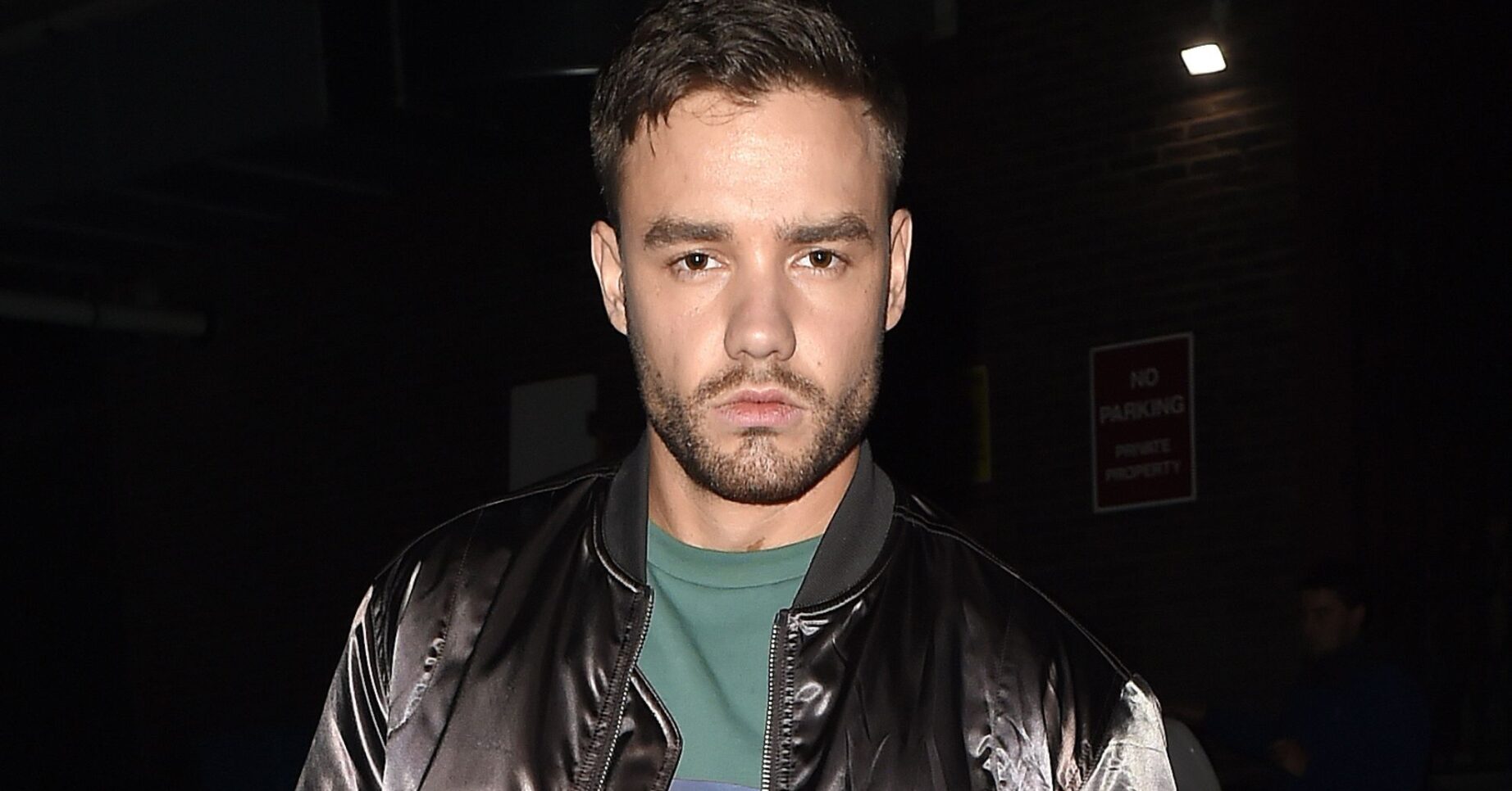 Liam Payne facing the camera dressed in black jacket and green t-shirt