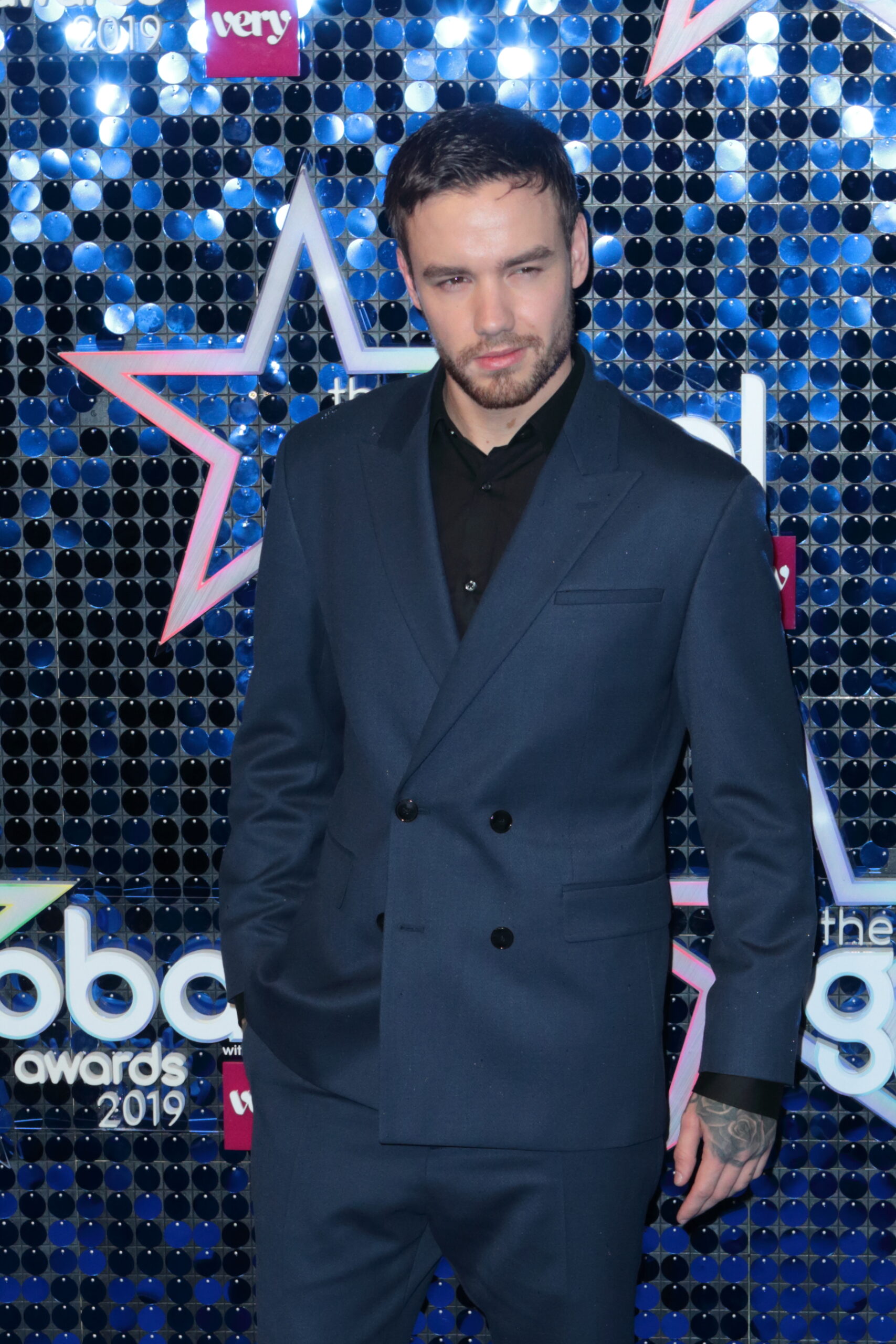Liam Payne in a navy suit in front of a glittery backdrop