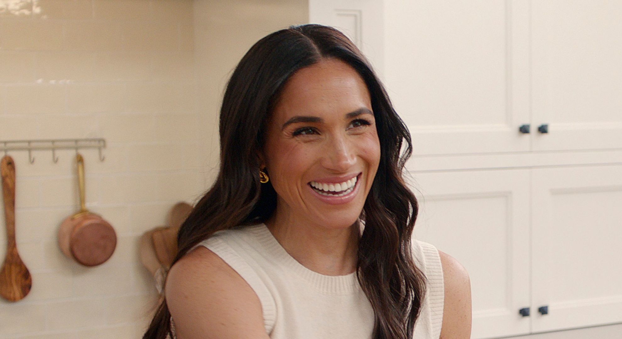 Meghan Markle smiling in her kitchen wearing a white outfit