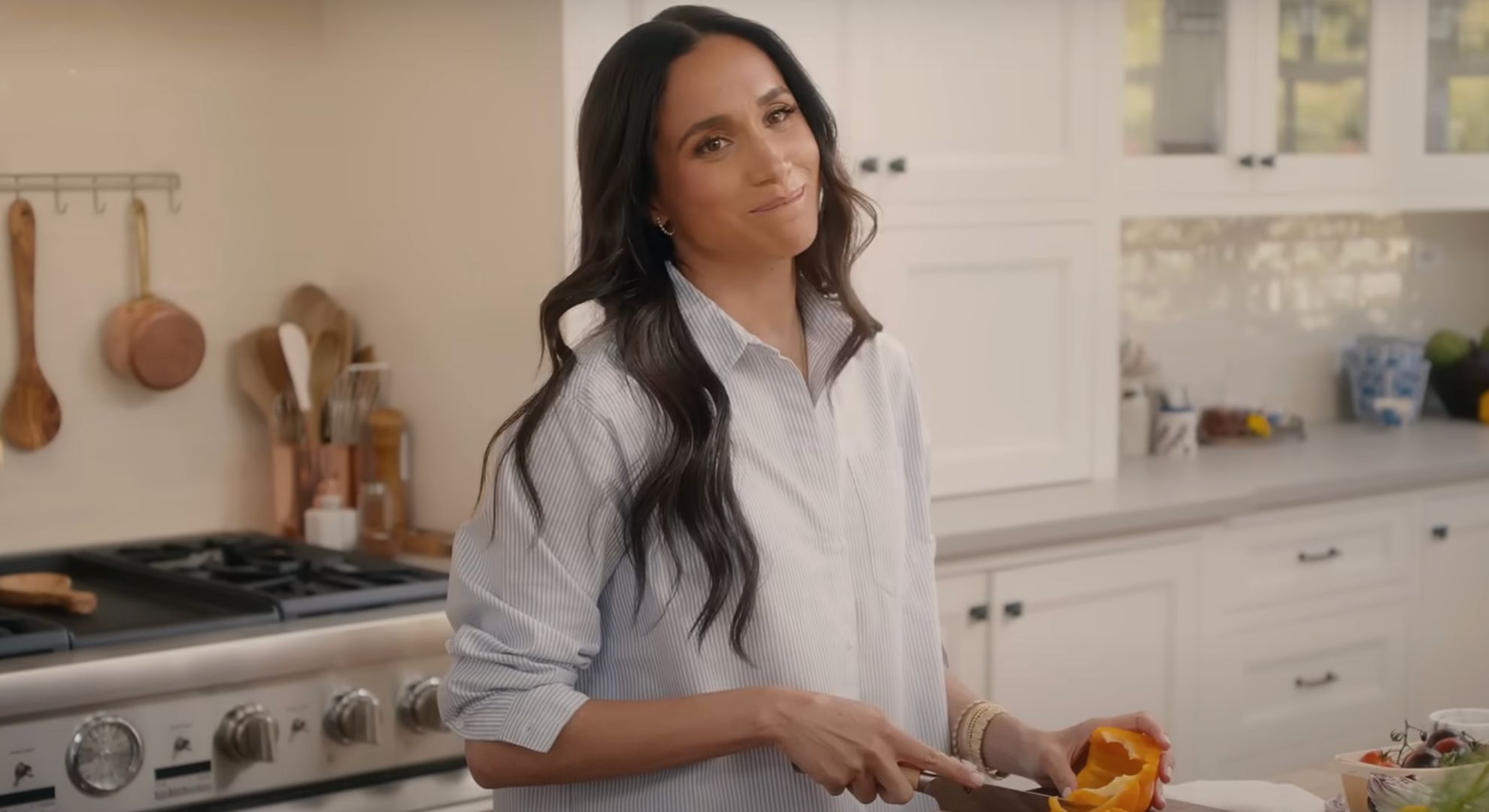 Meghan Markle wearing a blue shirt whilst chopping a pepper