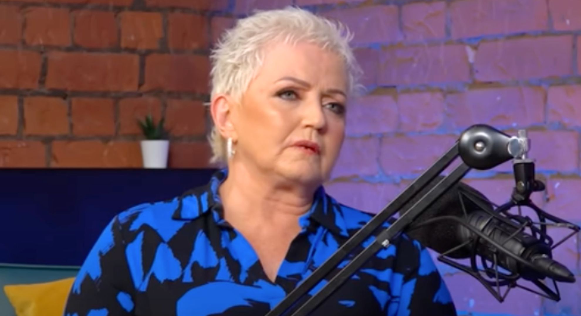 Linda Nolan wears a blue and black shirt as she speaks into a microphone