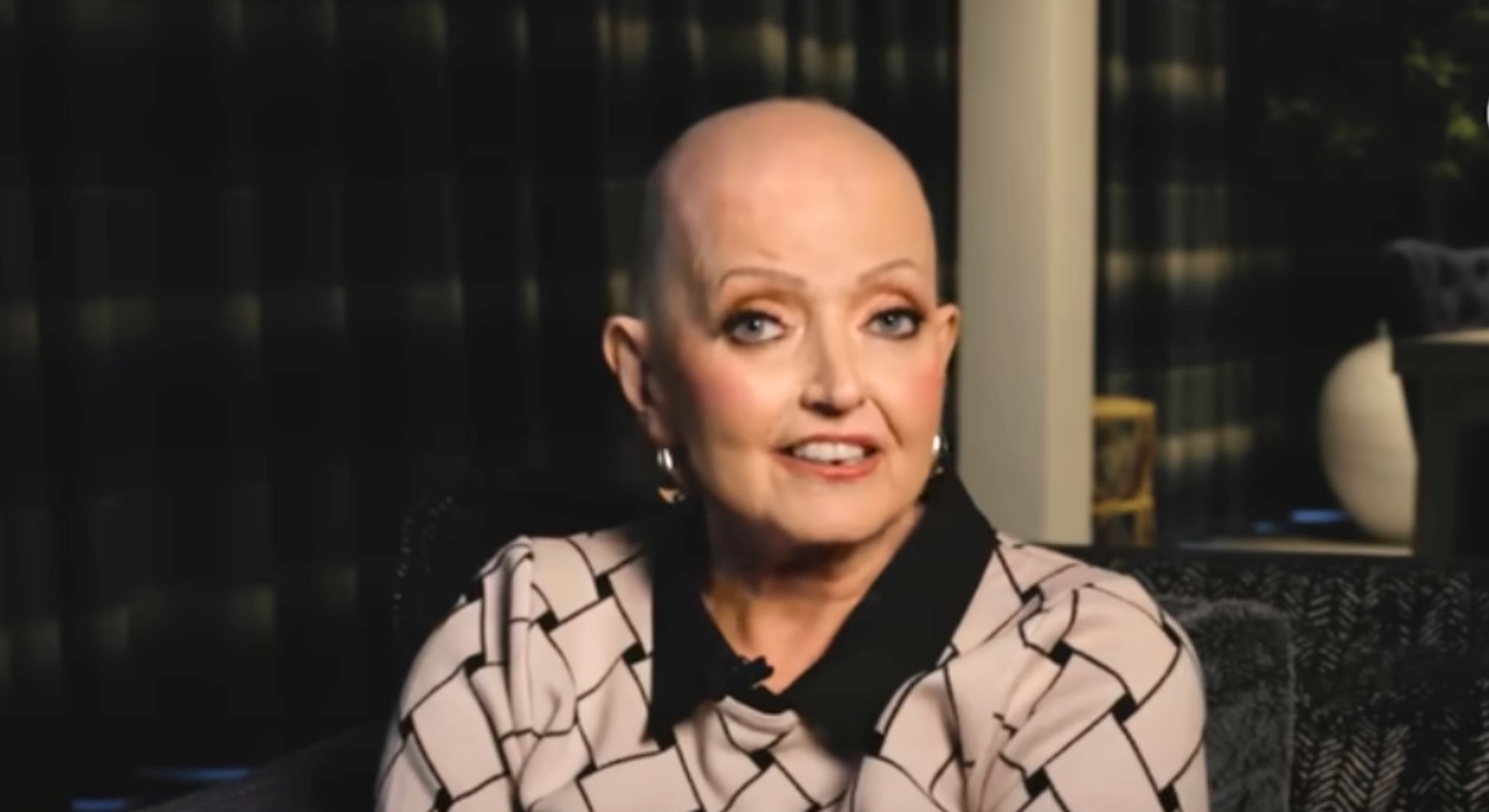 Linda Nolan wears a patterned shirt and sits on a sofa