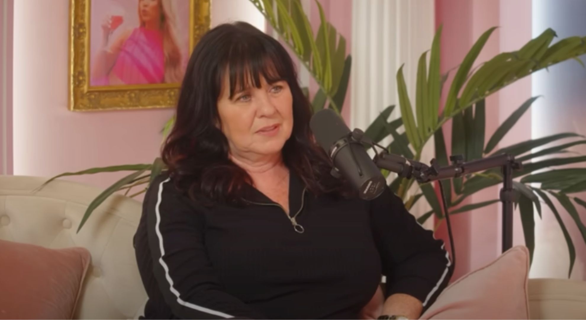 Coleen Nolan wears a black tracksuit and speaks into a microphone