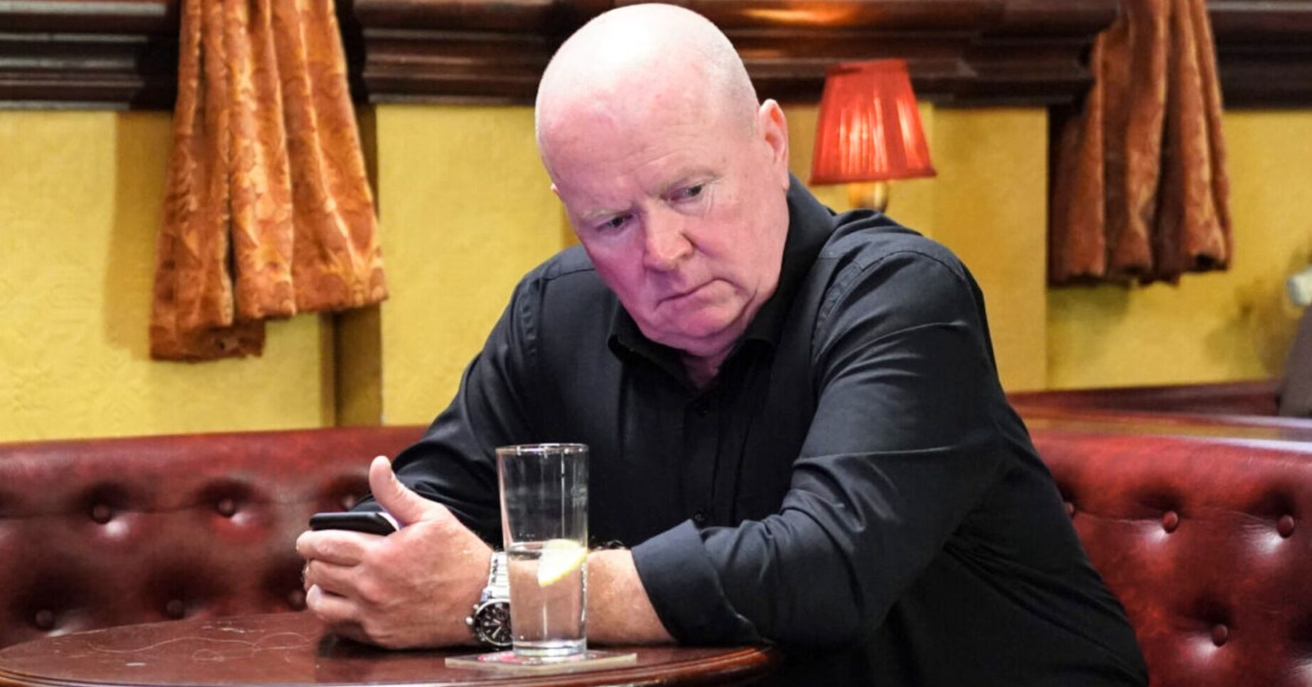 Phil looks miserable at the Vic on EastEnders (Credit: BBC/Composite: ED!)