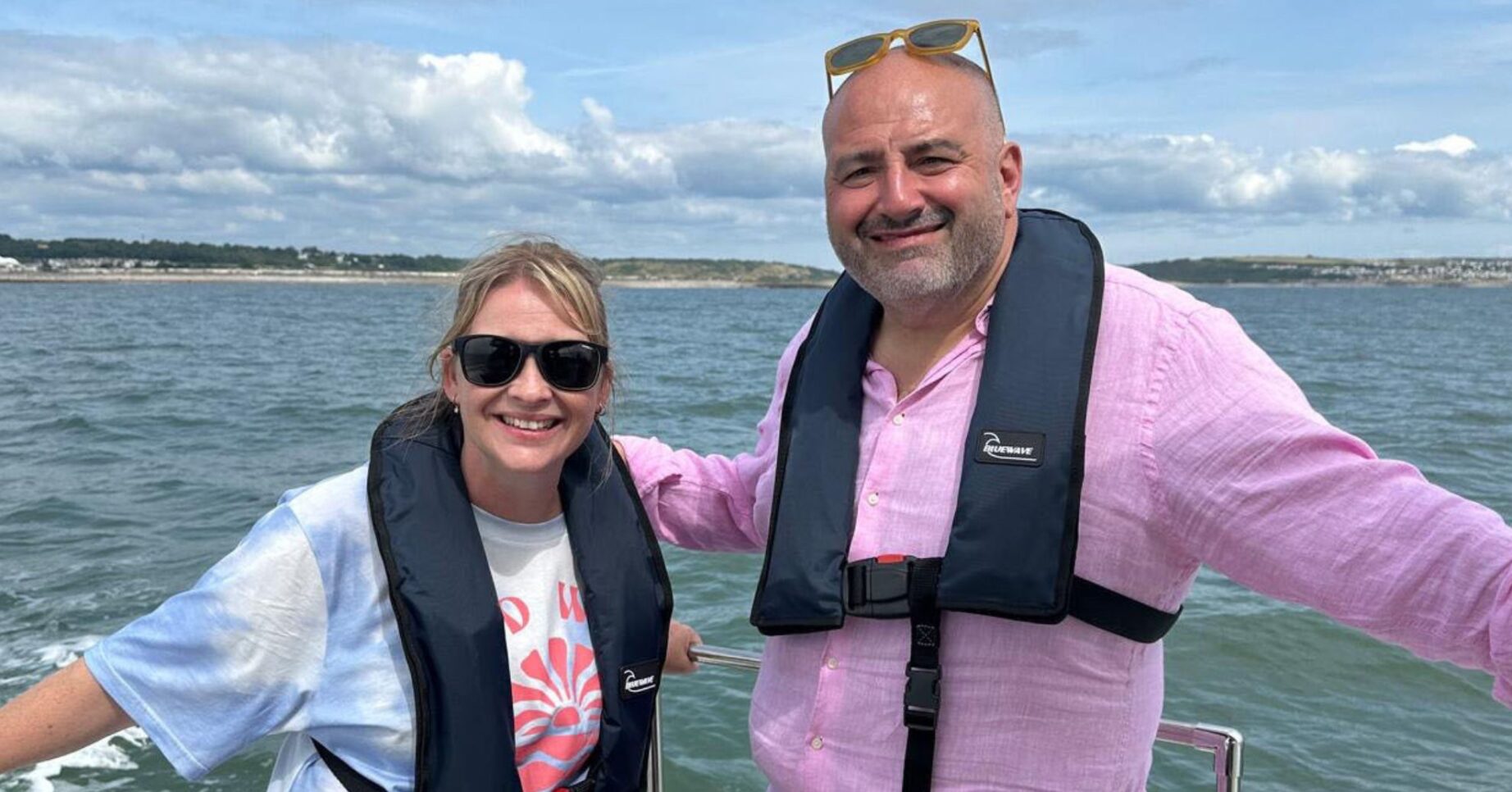Wynne and Joanna: All At Sea. They stand on boat on the sea smiling