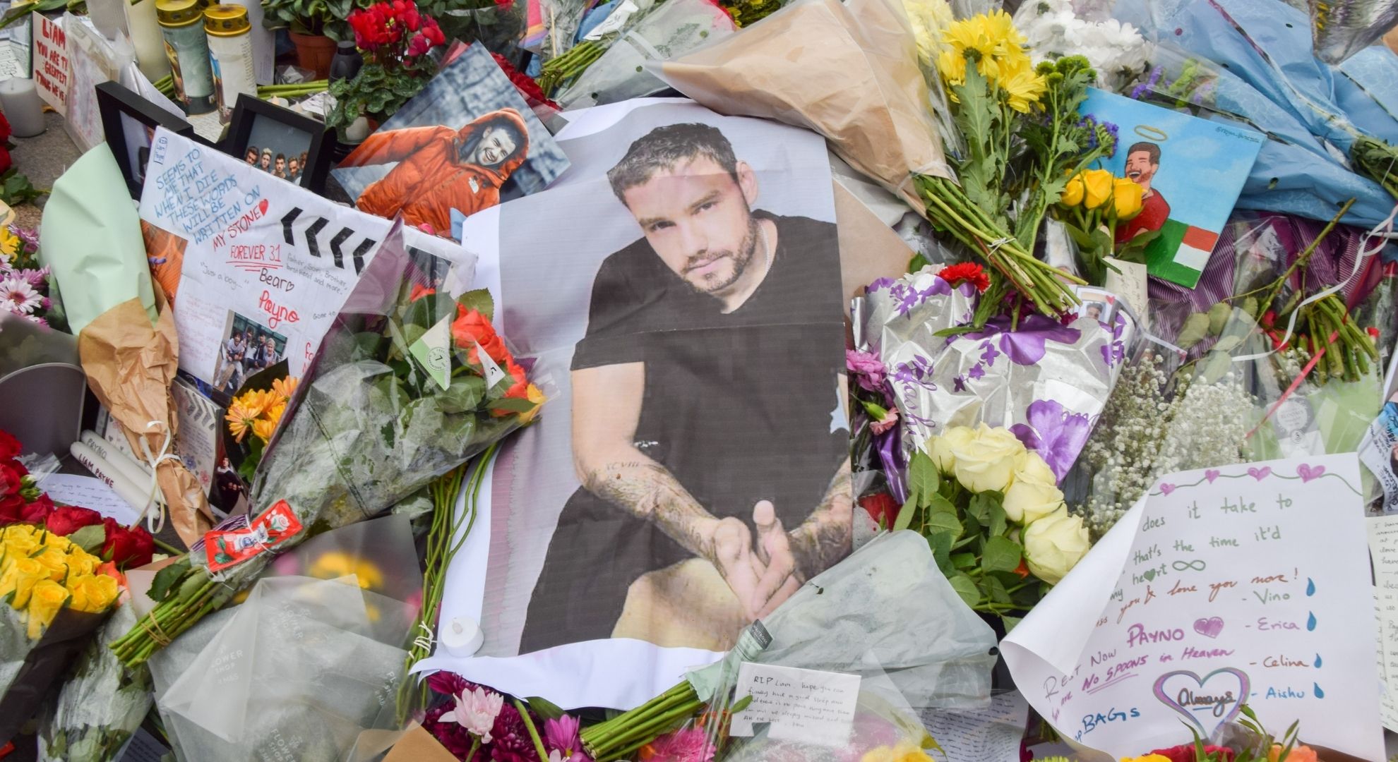 A memorial image of Liam Payne surrounded by flowers laid by fans
