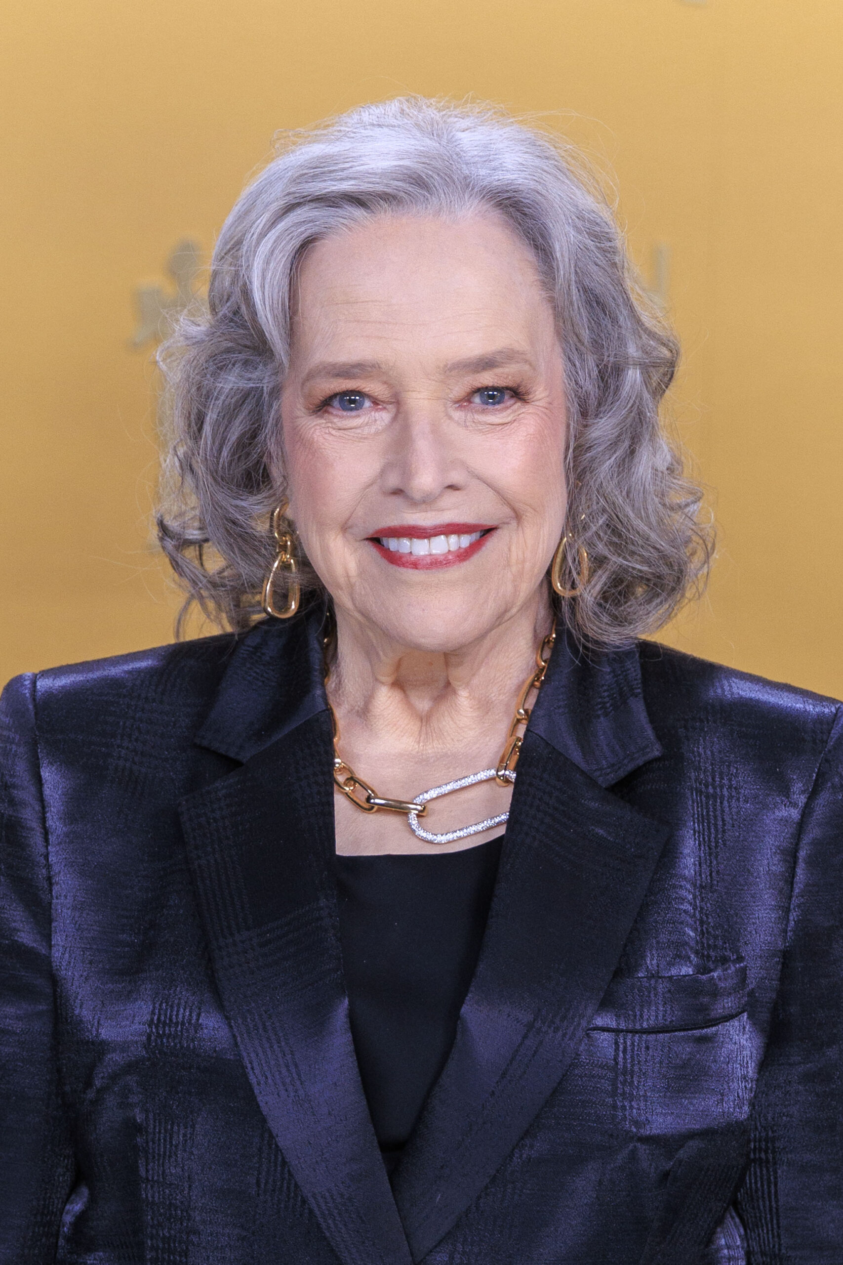 Kathy Bates smiling wearing a dark outfit