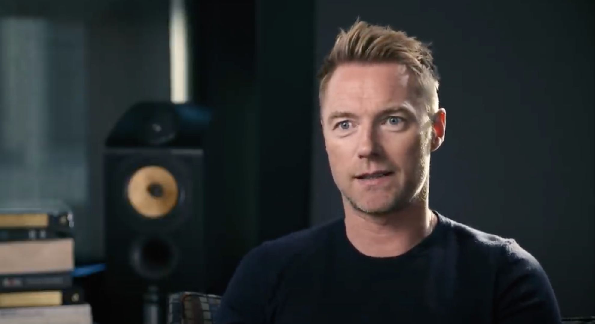 Ronan Keating wears a black t-shirt and sits in a recording studio
