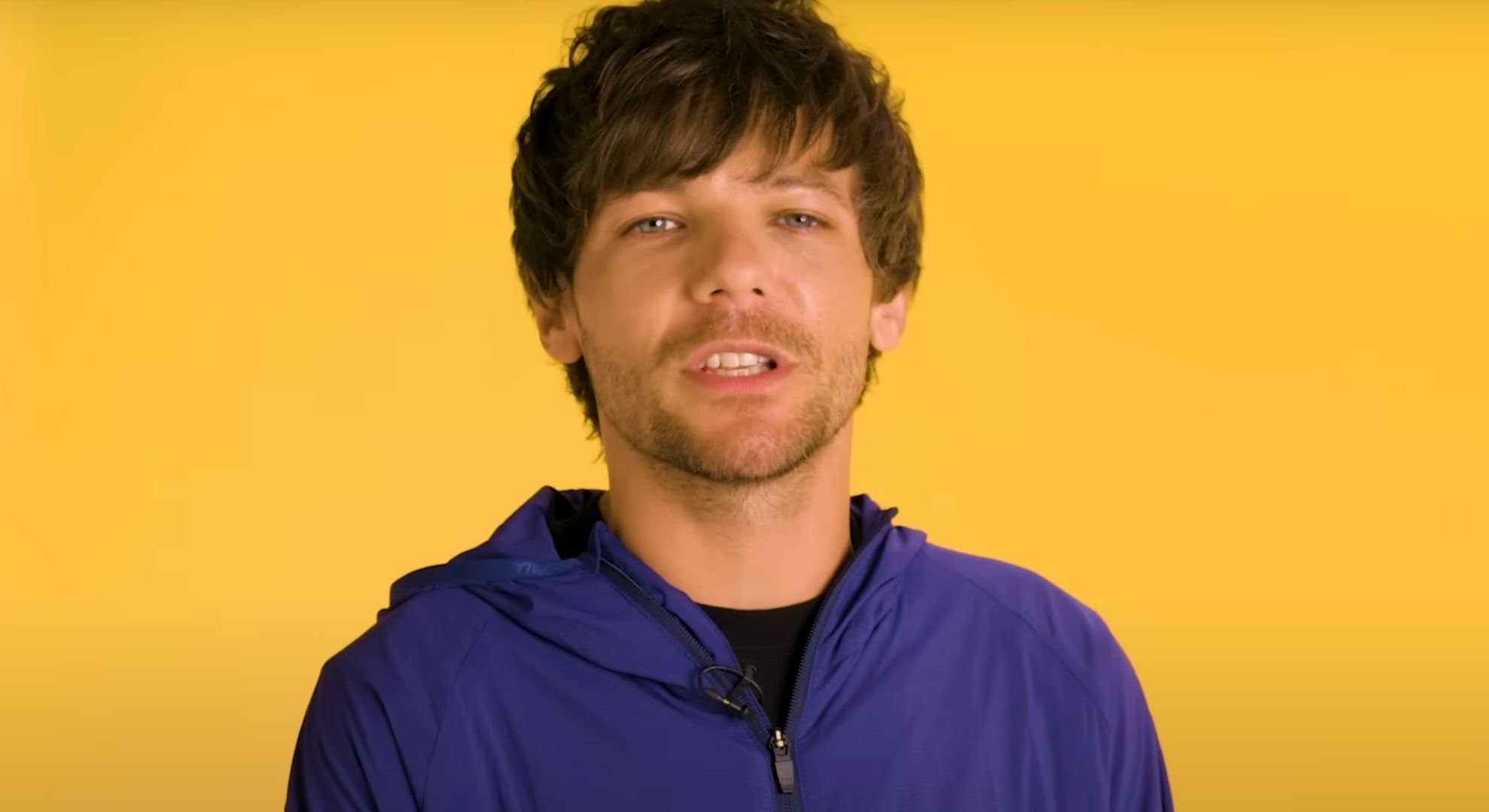 Louis Tomlinson on a yellow background speaking 