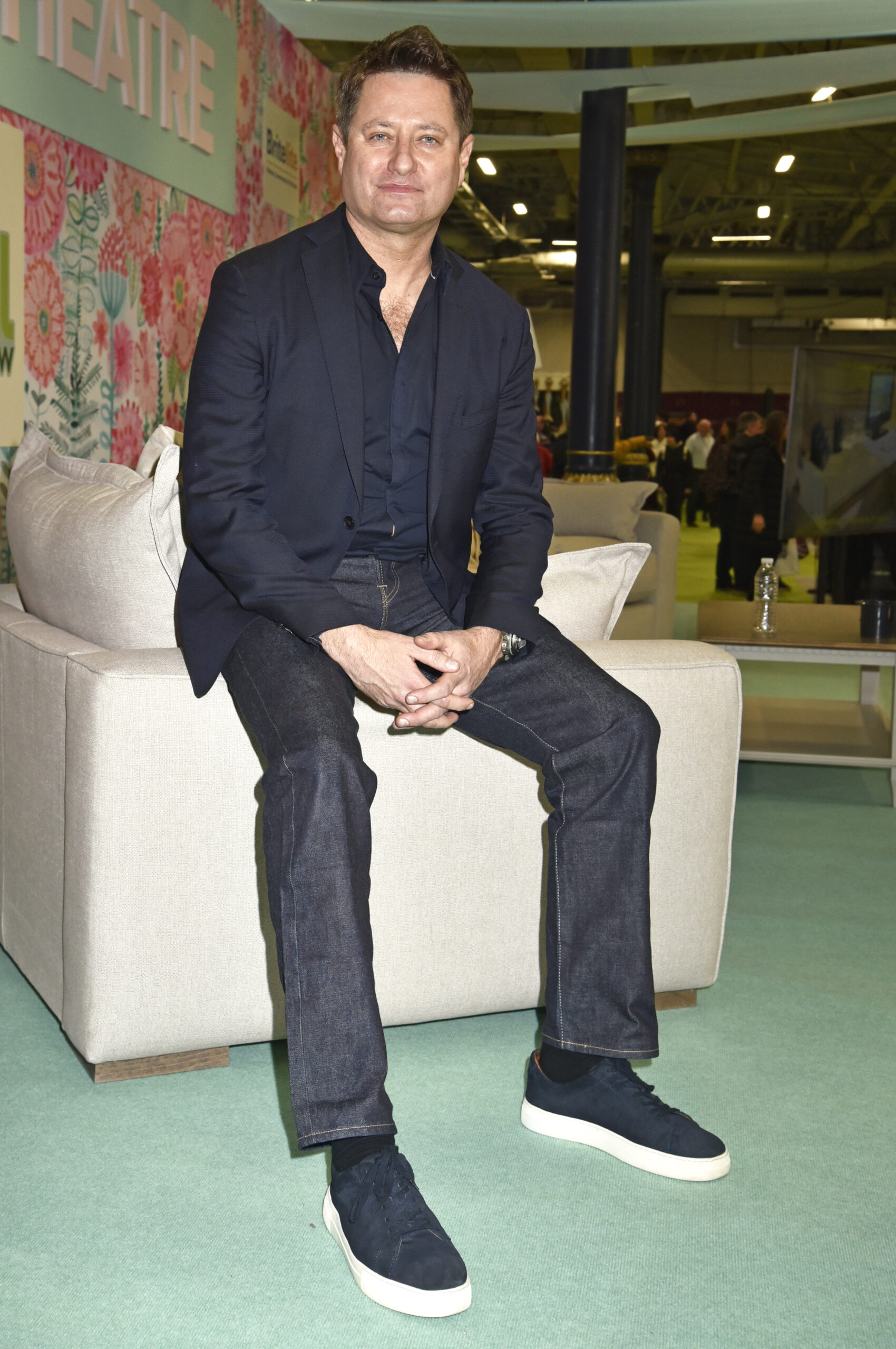 George Clarke smiling sitting on a white sofa
