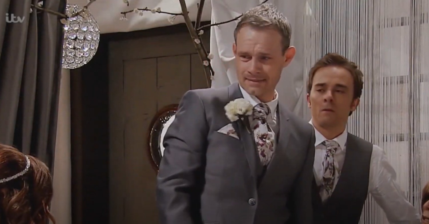Nick smiles at Carla at their wedding, with David standing in the background gormlessly