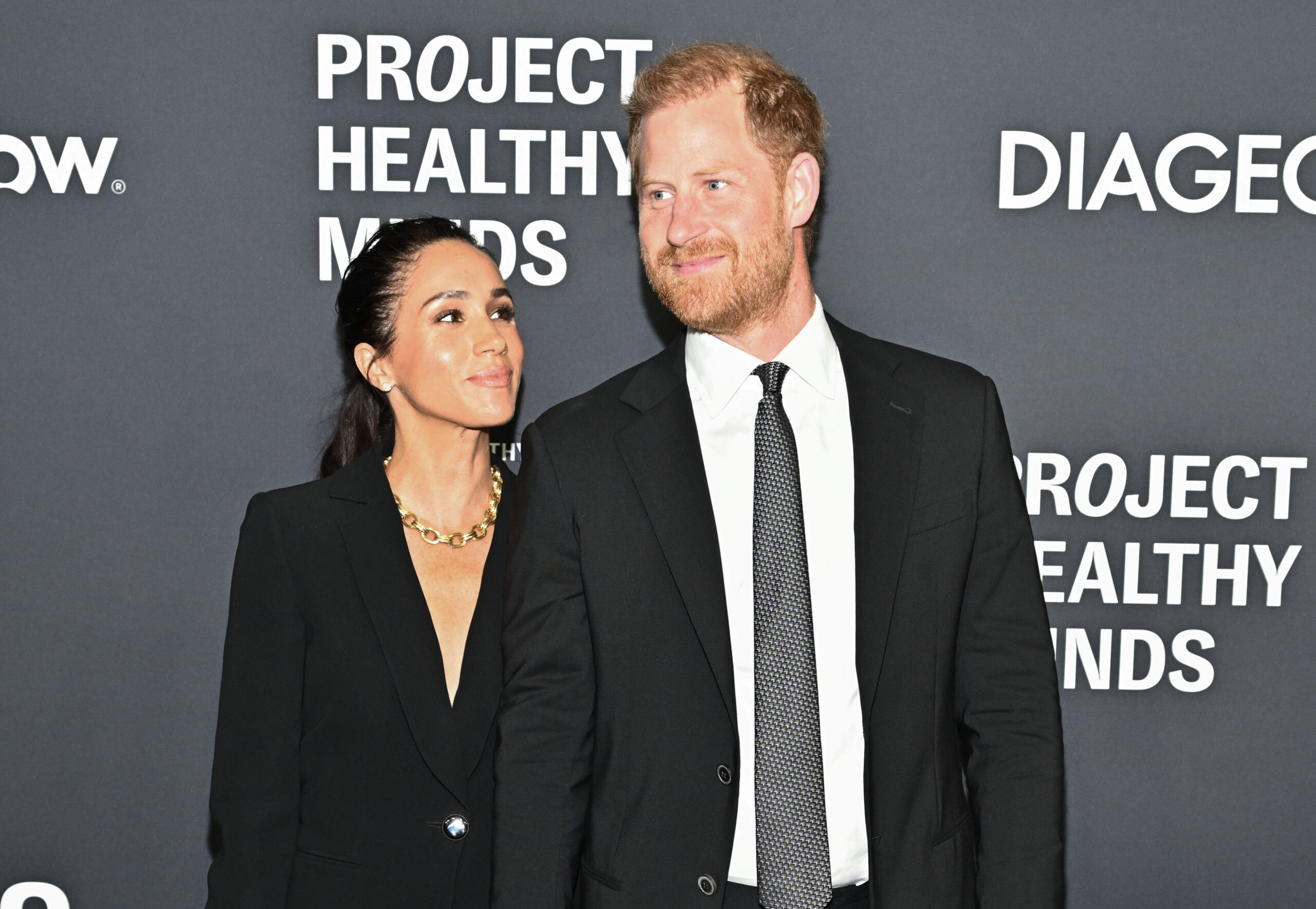 Meghan Markle smiling at Prince Harry on the red carpet at a charity gala