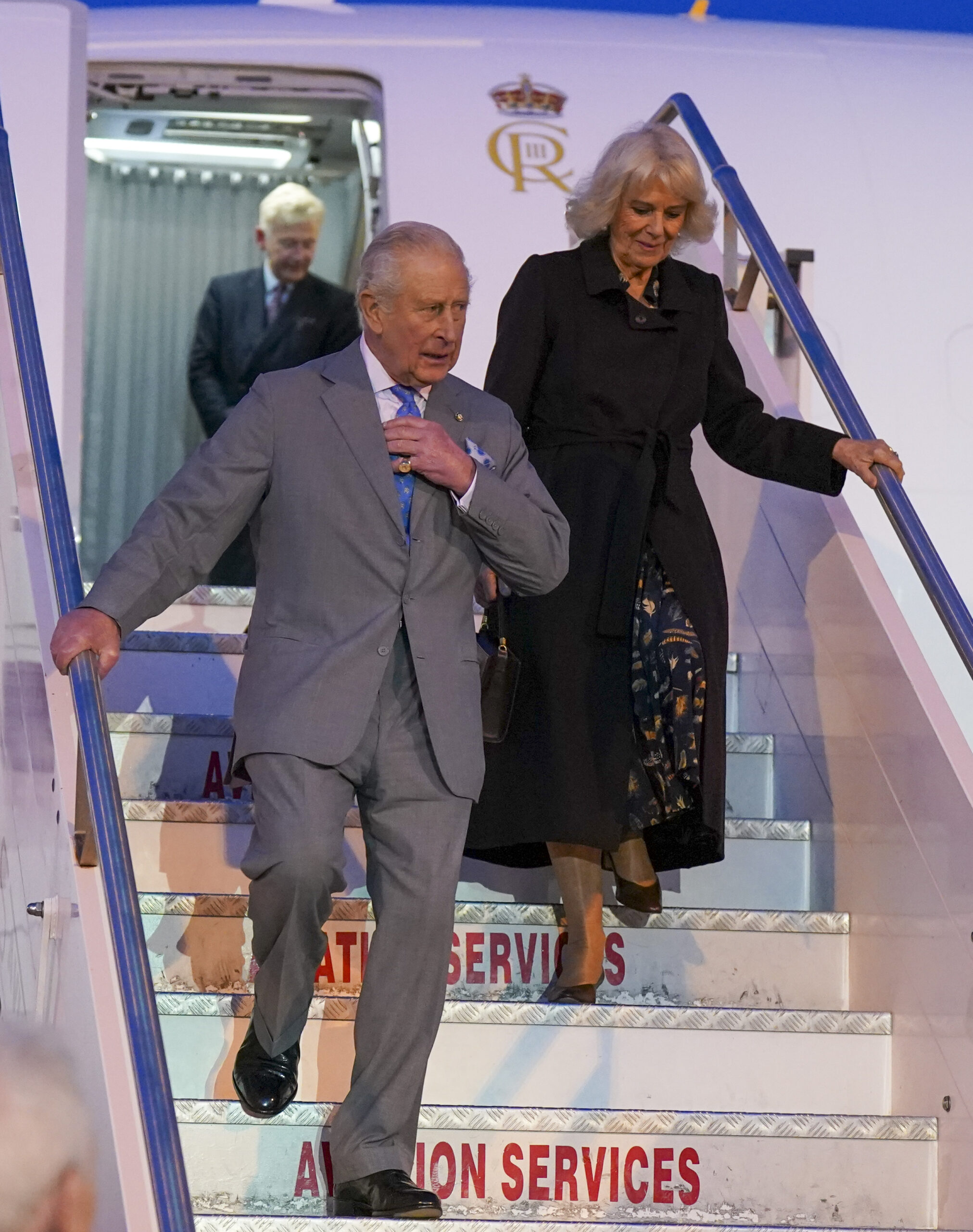 King Charles and Queen Camilla walking down the stairs of a plane
