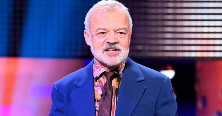 Talkshow host Graham Norton wearing a blue suit and patterned burgundy tie on set