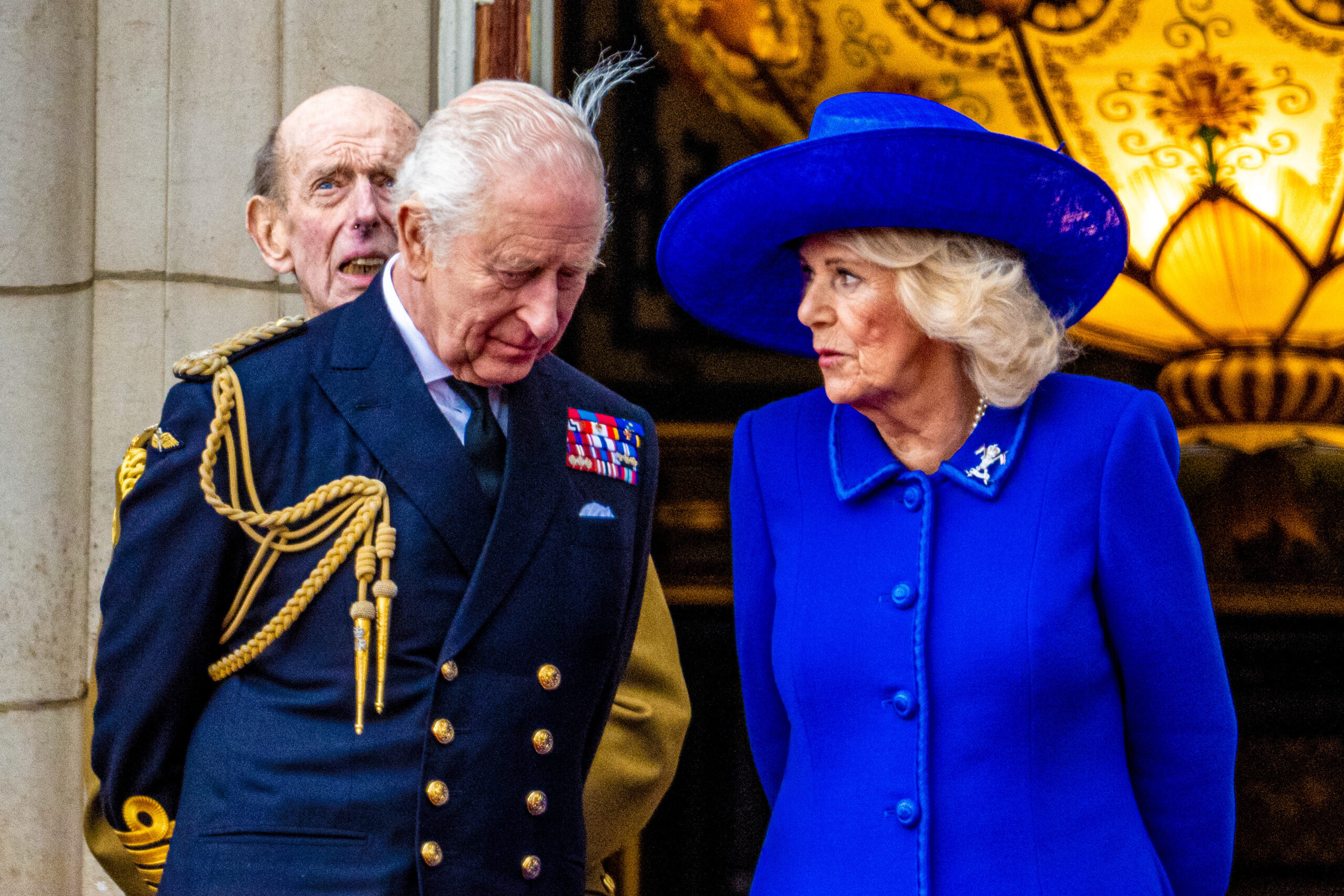 King Charles leaning in to Queen Camilla as she speaks to him