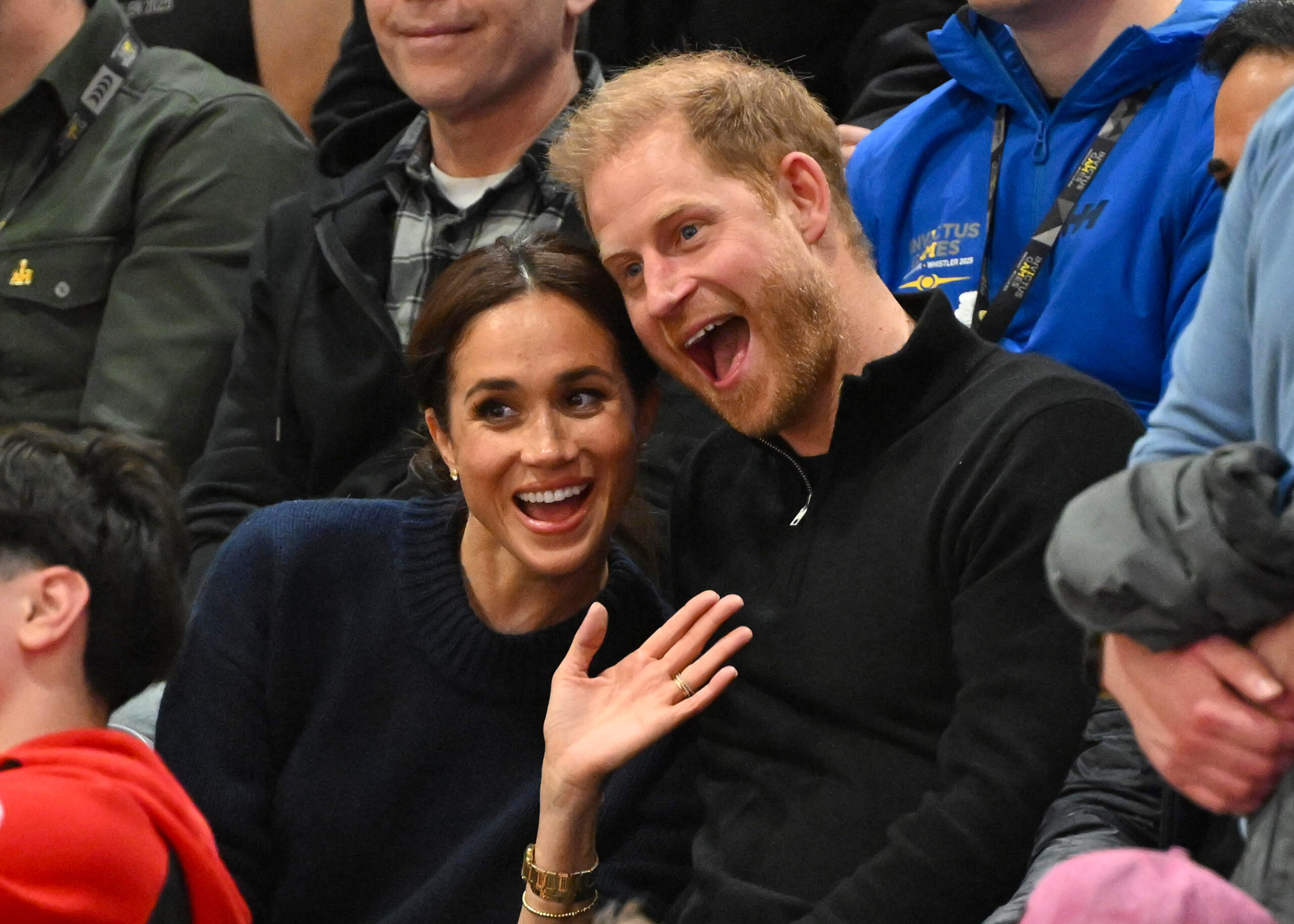 Meghan Markle and Prince Harry smiling, waving and leaning into eachother