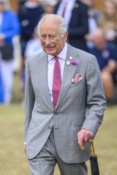 King Charles smiling and walking in grey suit