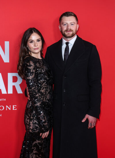 Holly Ramsay and Adam Peaty posing against a red wall