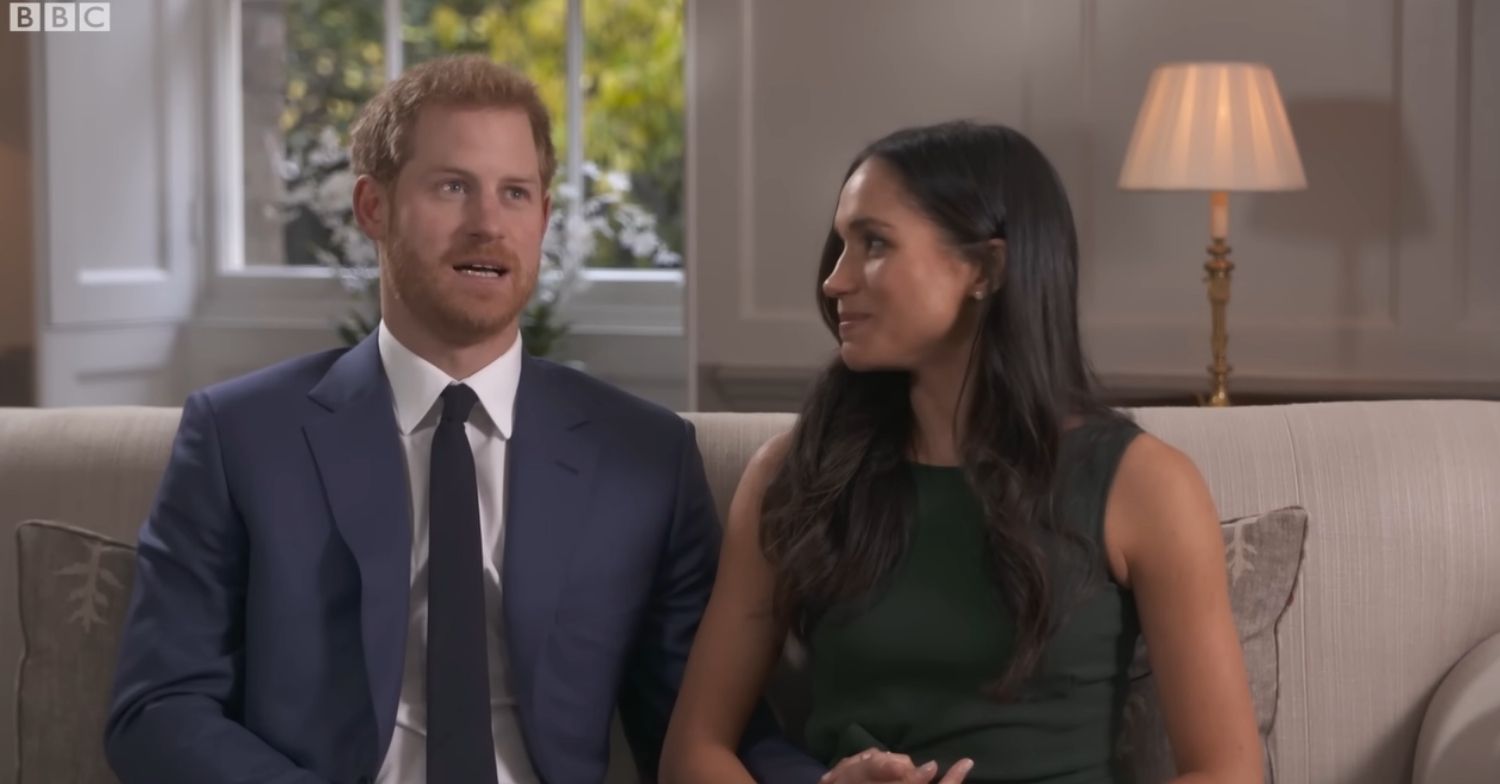 Prince Harry talking as Meghan Markle looks at him during engagement interview