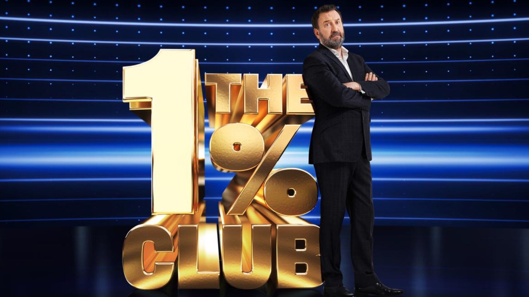 Lee Mack standing in front of The 1% Club logo