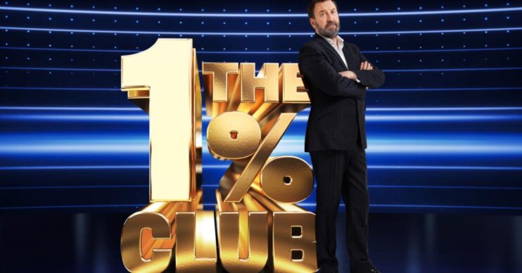 Lee Mack standing in front of The 1% Club logo