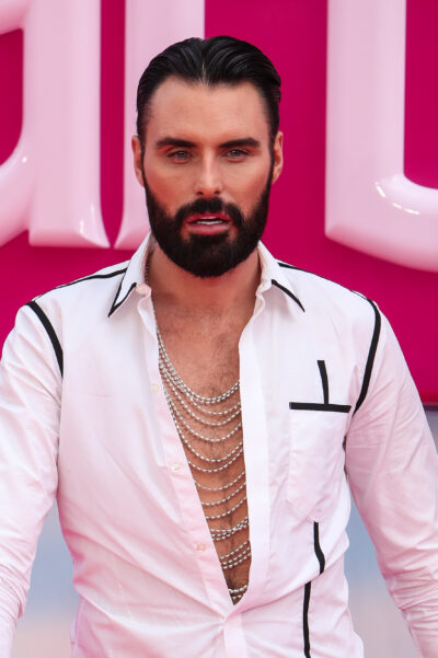 Rylan Clark wearing a white shirt standing against a pink background