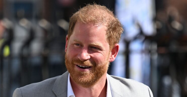 Prince Harry in grey blazer, smiling, during UK return