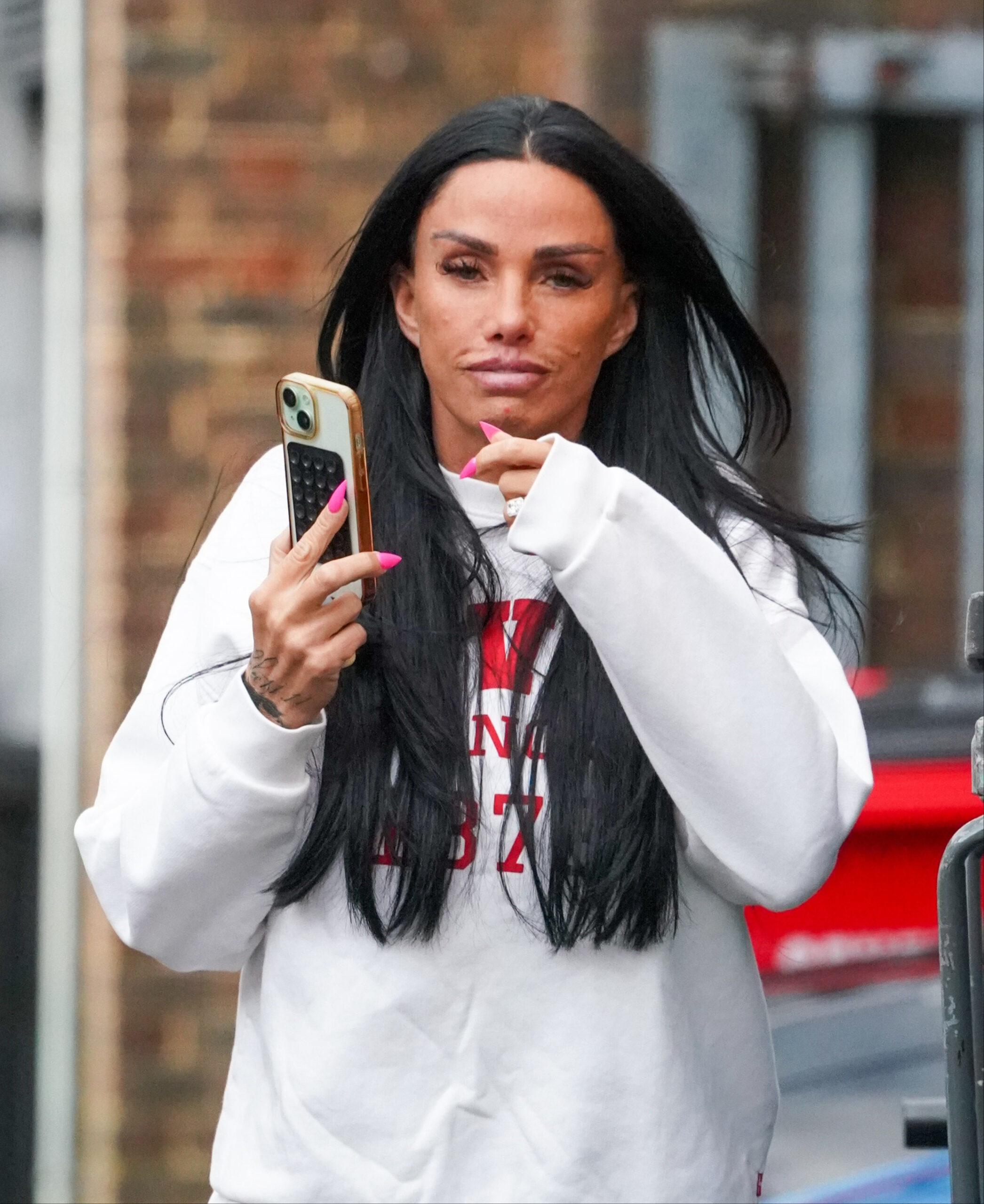 Katie Price walking in the street with her phone in hand 