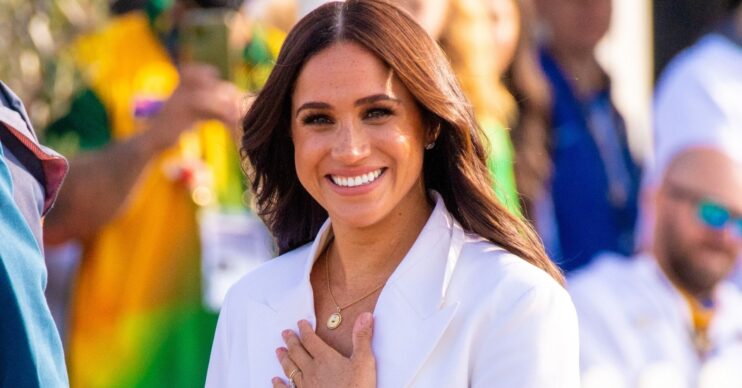 Meghan Markle smiling with her hand on her chest